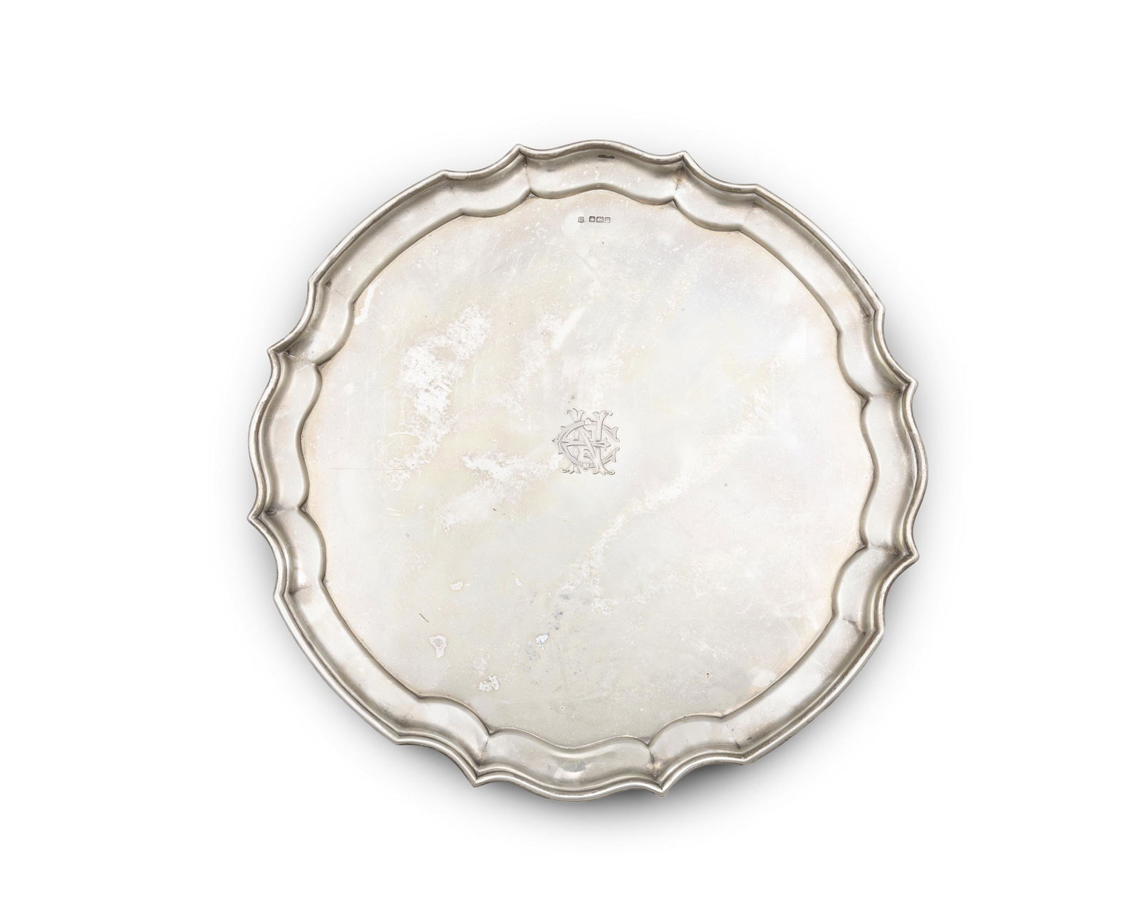 A GEORGE V SILVER SALVER Sheffield 1916, of shaped circular form with pie crust rim, engraved: A GEORGE V SILVER SALVER Sheffield 1916, of shaped circular form with pie crust rim, engraved initials and raised on four scroll feet (43 troy ozs). 35.3cm diameter
