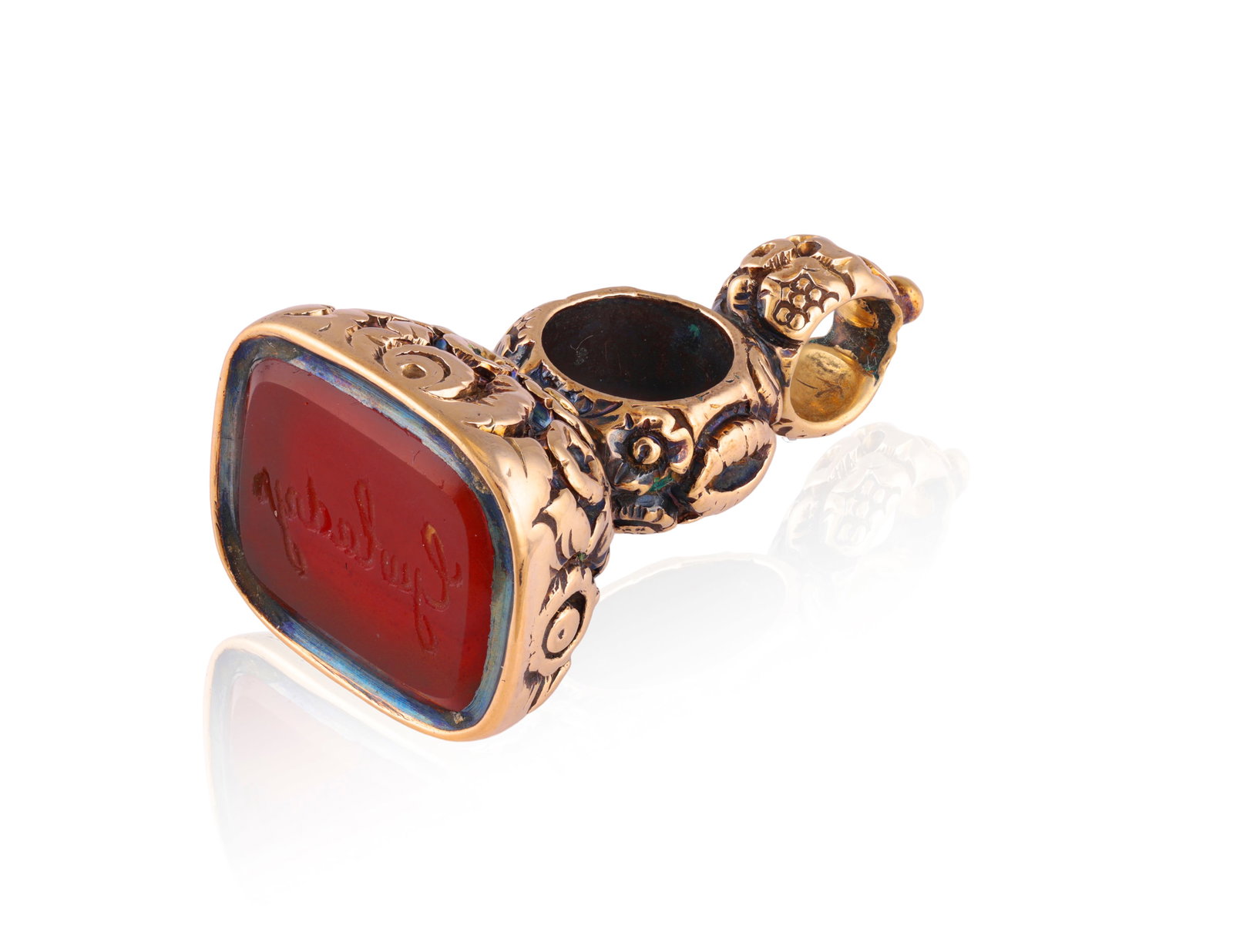 A FOB SEAL PENDANT Inset with a carnelian intaglio spelling out ‘Gwladys’ for ‘Saint: A FOB SEAL PENDANT Inset with a carnelian intaglio spelling out ‘Gwladys’ for ‘Saint Gladys’, to a mount with scrolled foliate motifs, mounted in 9K gold, length 2.7cm * This lot is sold witho