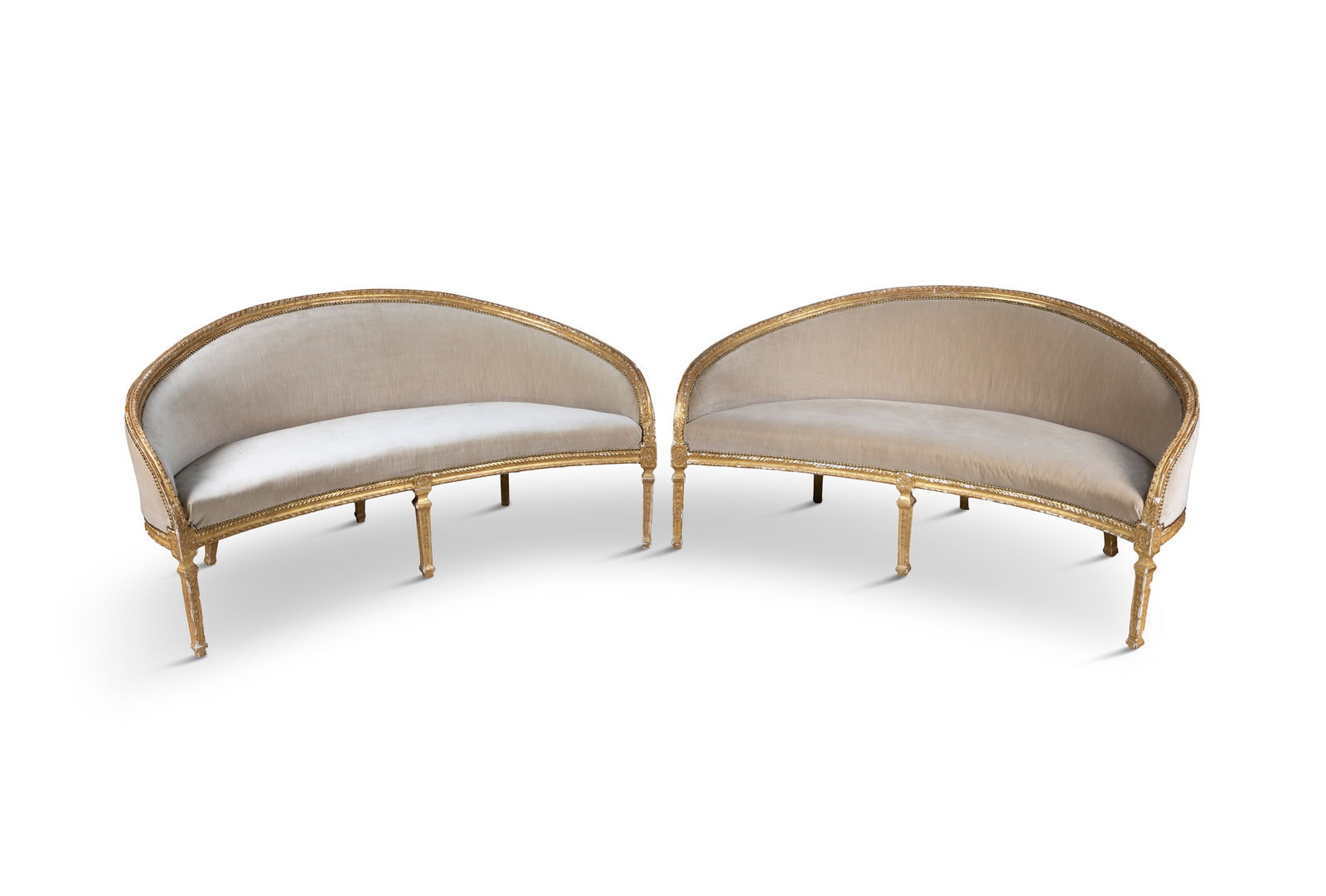 A PAIR OF ENGLISH GILTWOOD CRESCENT SHAPED SETTEES, 19TH CENTURY each with squab cushions and: A PAIR OF ENGLISH GILTWOOD CRESCENT SHAPED SETTEES, 19TH CENTURY each with squab cushions and upholstered in close nailed beige fabric, the frames carved with ribbon wrapped decoration, raised on squa