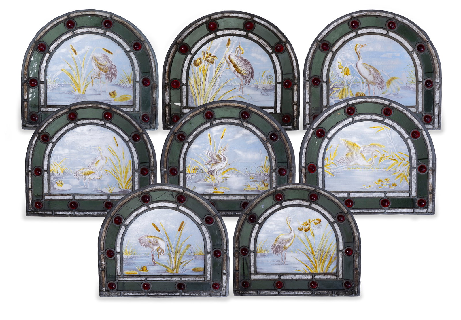 A SET OF EIGHT GLAZED AND LEADED ARCHED PANELS, LATE 19TH CENTURY, each hand-painted with scenes: A SET OF EIGHT GLAZED AND LEADED ARCHED PANELS, LATE 19TH CENTURY, each hand-painted with scenes of wading birds by the waterside in shades of blue and pink, interspersed with red glass cabochons, 38c