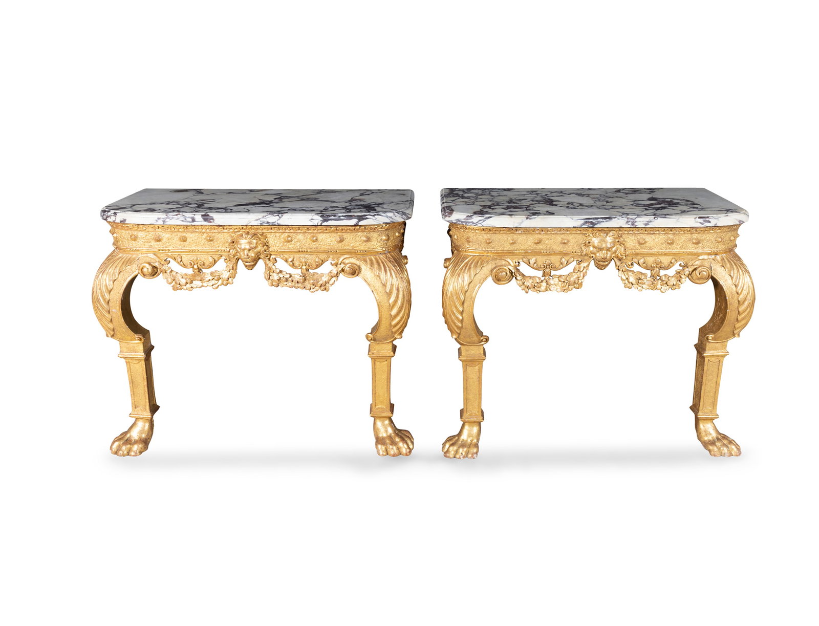 A PAIR OF IRISH GEORGE II GILTWOOD CONSOLE TABLES, WITH LATER ASSOCIATED MARBLE TOPS, the sanded: A PAIR OF IRISH GEORGE II GILTWOOD CONSOLE TABLES, WITH LATER ASSOCIATED MARBLE TOPS, the sanded frieze boldly carved with lion mask and floral garlands, on robust acanthus capped knees and large paw 