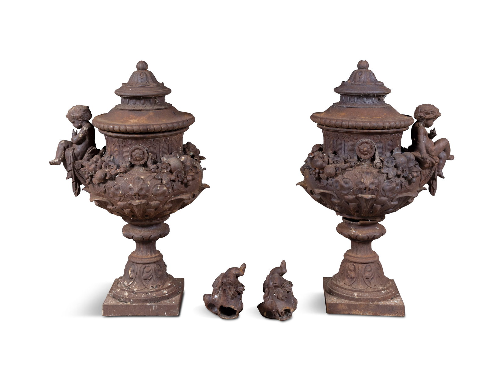 A PAIR OF CAST IRON GARDEN URNS AND COVERS, the covers surmounted with finials, over profusely: A PAIR OF CAST IRON GARDEN URNS AND COVERS, the covers surmounted with finials, over profusely decorated baluster shaped bodies, each with twin putti carrying handles (two partially detached), on wais