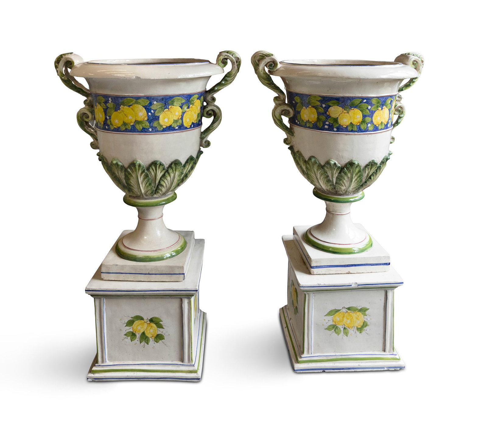 A PAIR OF LARGE ITALIAN CERAMIC LEMON TREE URNS, each with double twin handles in a cream glaze,: A PAIR OF LARGE ITALIAN CERAMIC LEMON TREE URNS, each with double twin handles in a cream glaze, with central band of lemons against a blue ground above foliate decoration in high relief, on socle bas