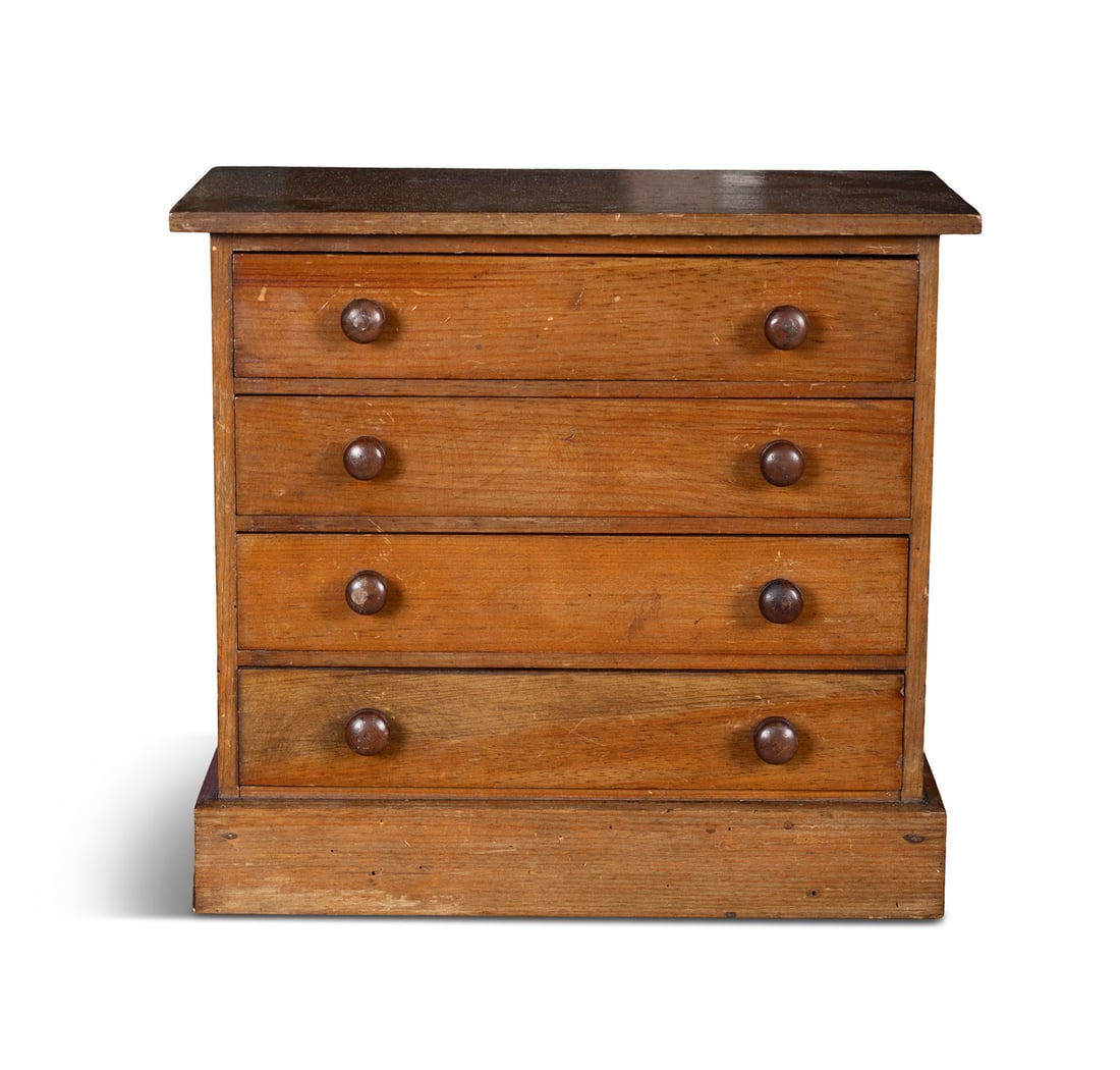 A MINIATURE STAINED PINE SPECIMEN CABINET, in the form of a chest of drawers on an outset plinth (1 of 3)