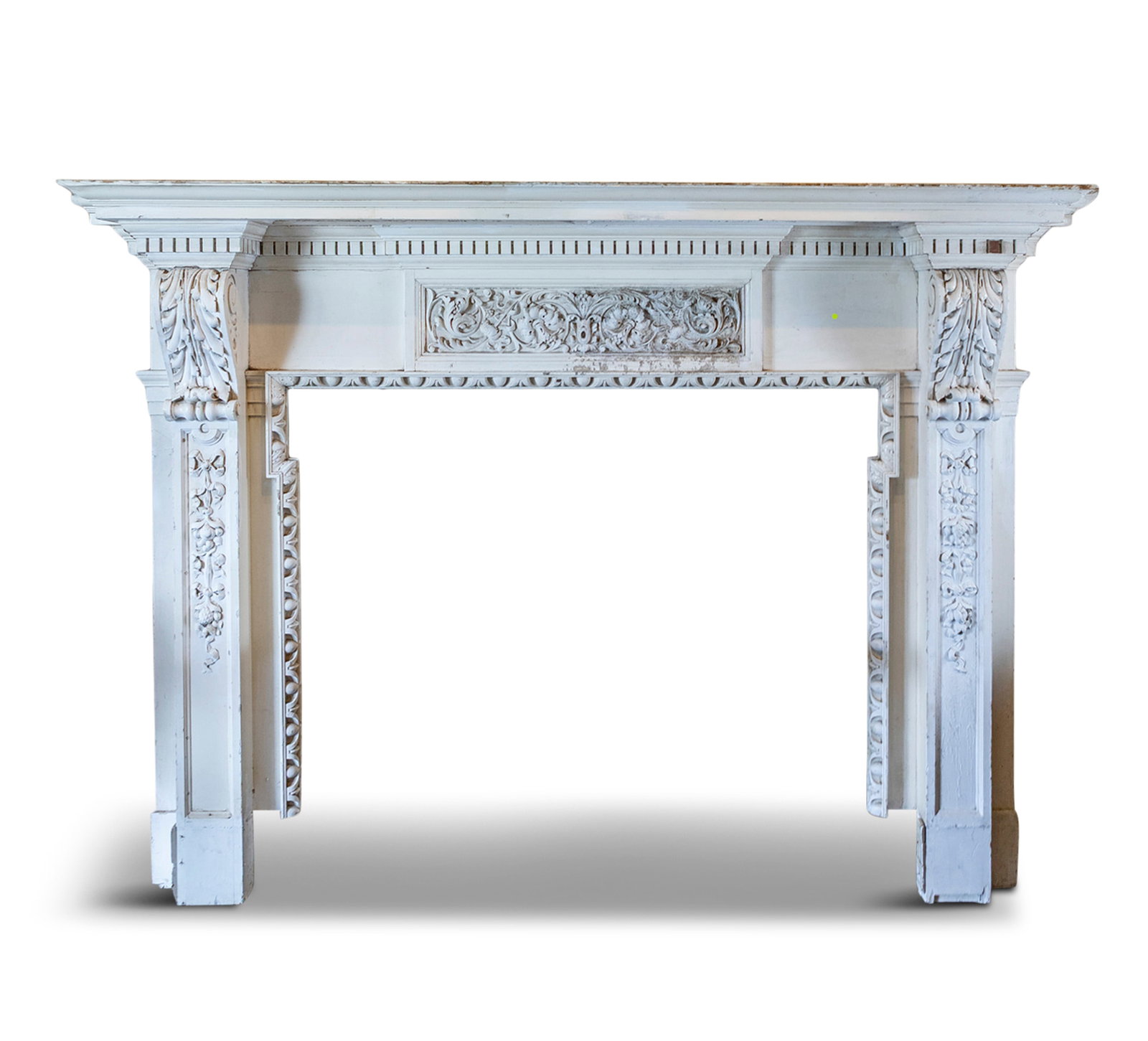 A WHITE PAINTED TIMBER FIREPLACE outset moulded mantel over dentil frieze and centred with a: A WHITE PAINTED TIMBER FIREPLACE outset moulded mantel over dentil frieze and centred with a scrollwork cartouche, flanked by acanthus carved corbels, pilasters with carved ribbon tied swags, the inte
