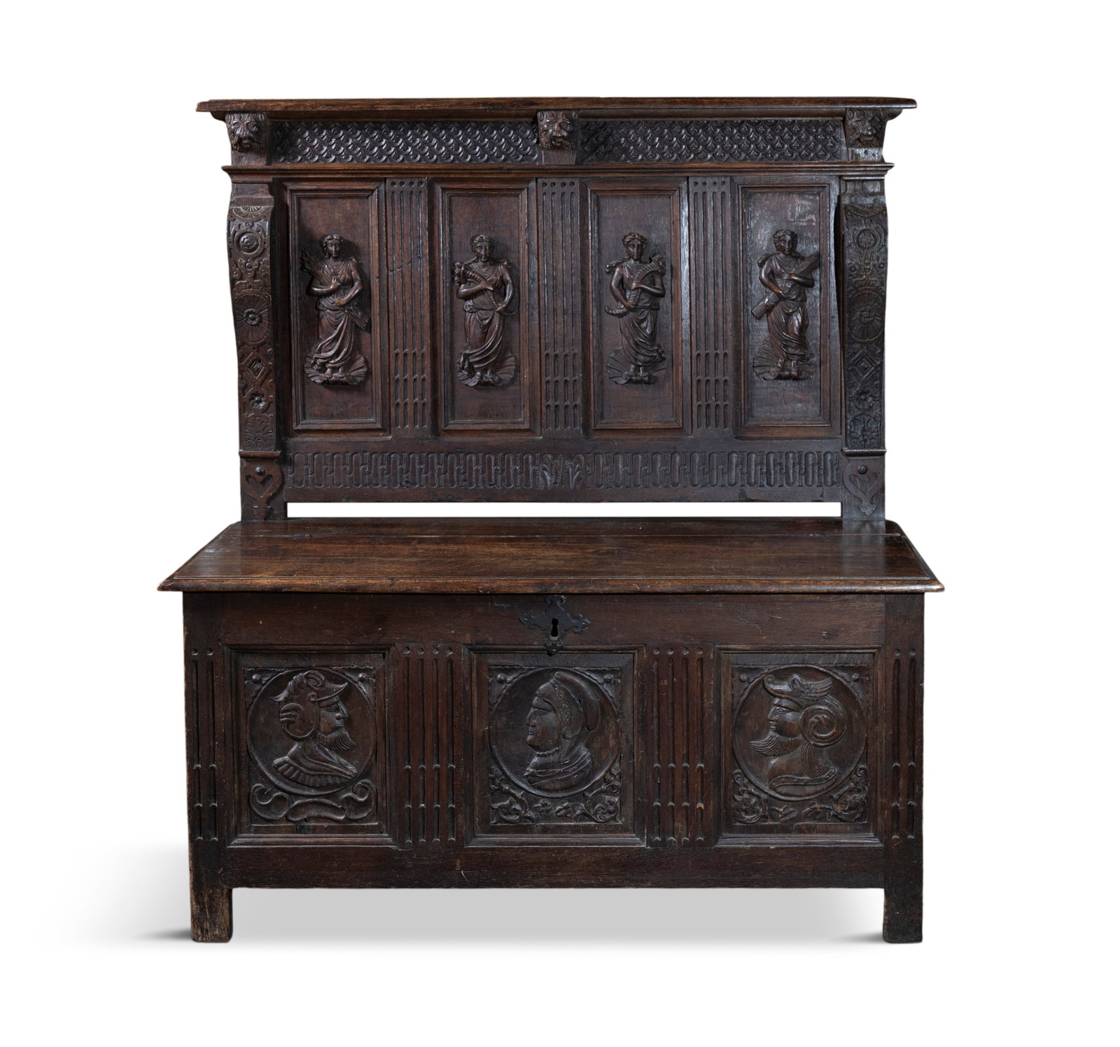 A 19TH CENTURY OAK MONKS BENCH, the upright panel back carved with the four graces flanked by: A 19TH CENTURY OAK MONKS BENCH, the upright panel back carved with the four graces flanked by fluted pilasters, carved corbels to each end over a solid panel lift top seat over carved base with depict