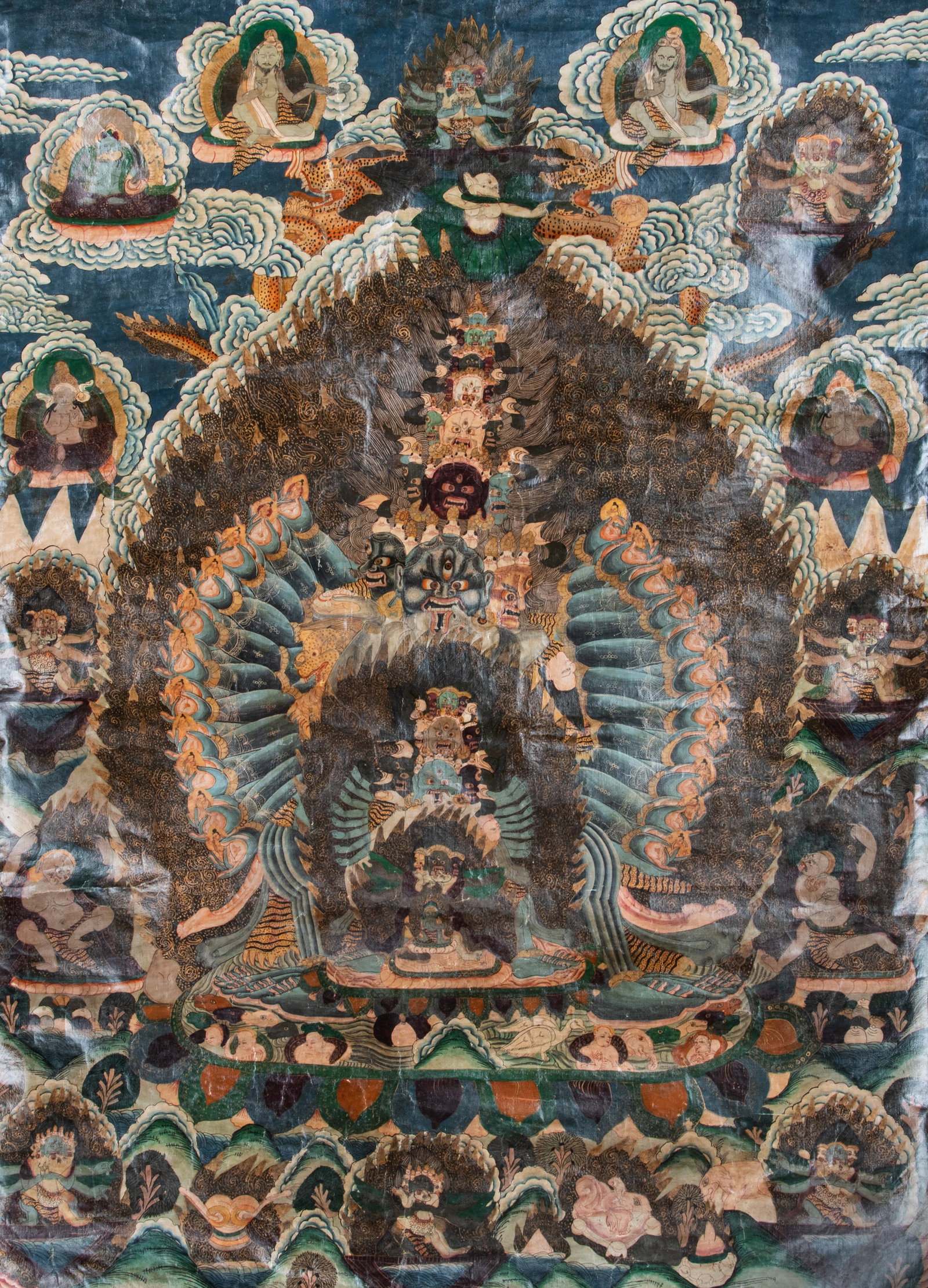 A POLYCHROME THANGKA ON CLOTH DEPICTING A MULTI-HEADED AND ARMED TANTRIC DEITY GUHYAGARBHA /: A POLYCHROME THANGKA ON CLOTH DEPICTING A MULTI-HEADED AND ARMED TANTRIC DEITY GUHYAGARBHA / MAHAJALA Nepal, 20th Century. With a purple silk brocade framing This powerful thangka depicts the wrathful