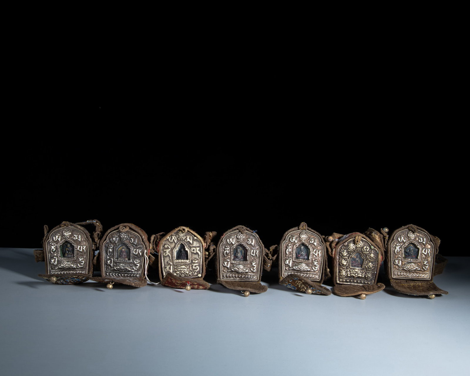 A SET OF SEVEN MINIATURE SHRINE-SHAPED MIXED-METAL GAU BOXES WITH THEIR CONTENTS AND CLOTH COVERS: A SET OF SEVEN MINIATURE SHRINE-SHAPED MIXED-METAL GAU BOXES WITH THEIR CONTENTS AND CLOTH COVERS Tibet or Nepal, first half of 20th century H.7.5-8.2cm Provenance: from the collection of a prominent 