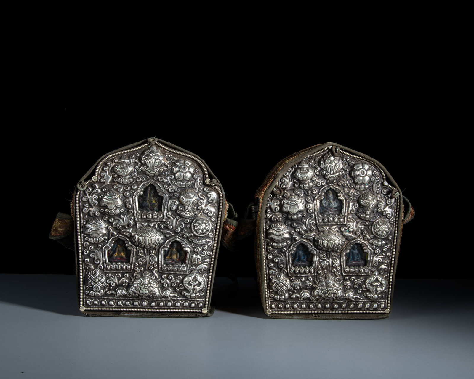 A RARE PAIR OF SHRINE-SHAPED SILVERED MIXED-METAL GAU BOXES WITH THEIR CONTENTS AND CLOTH COVERS: A RARE PAIR OF SHRINE-SHAPED SILVERED MIXED-METAL GAU BOXES WITH THEIR CONTENTS AND CLOTH COVERS Tibet or Nepal, first half of 20th century The silver casing of the portable shrine (Gau) is elaboratel
