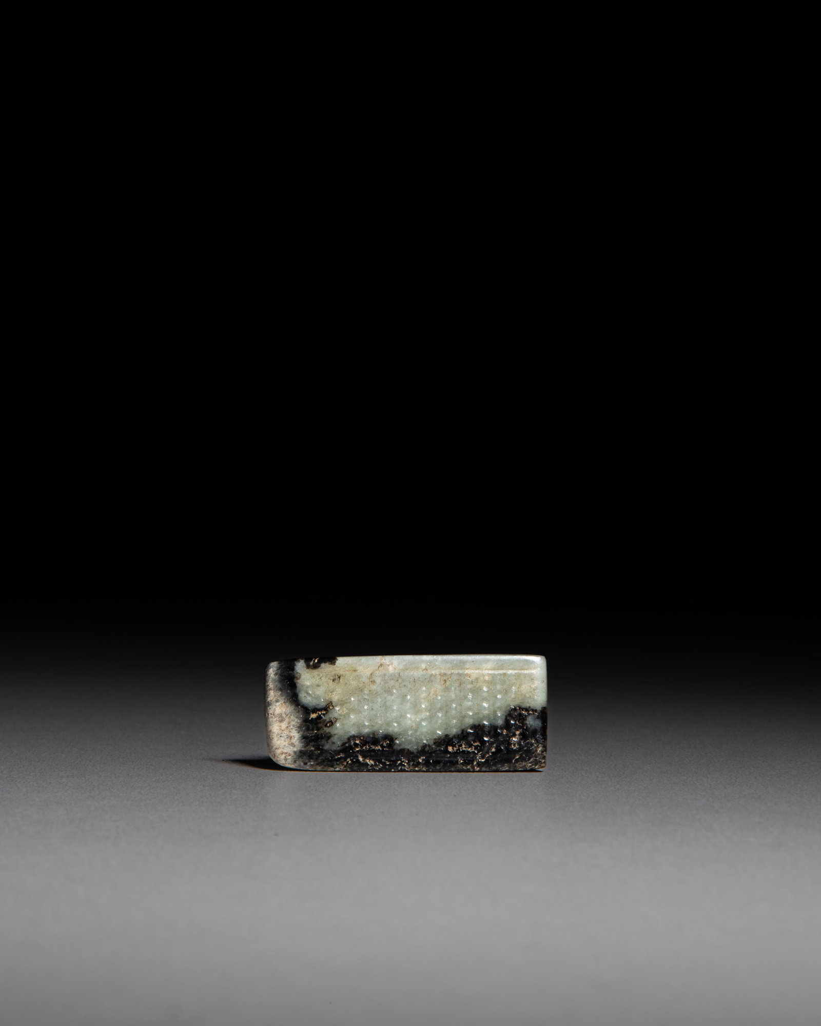A CELADON AND BLACK JADE SWORD SLIDE CARVED WITH LOW-RELIEF BOSSES. 汉代 青 (1 of 3)