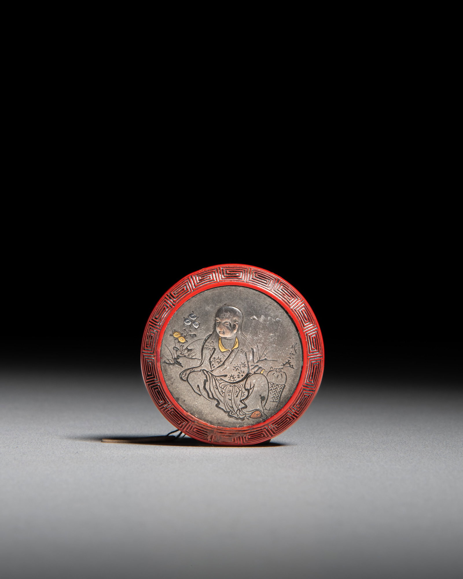 A CARVED TSUISHU CINNABAR LACQUER WITH GOLD, SILVER AND COPPER INLAID MANJU NETSUKE, SIGNED Japan, (1 of 2)