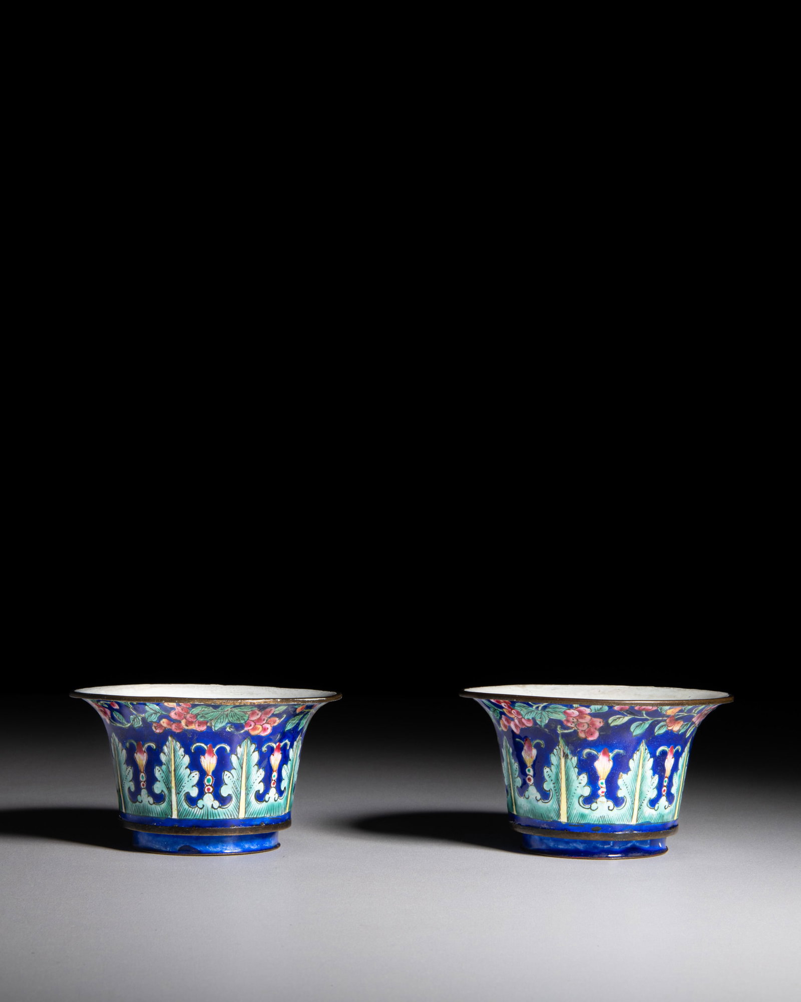 A PAIR OF PAINTED ENAMEL CUPS WITH A BLUE GROUND DECORATED WITH COLOURFUL ROSES, FRUITS AND LEAVES (1 of 2)