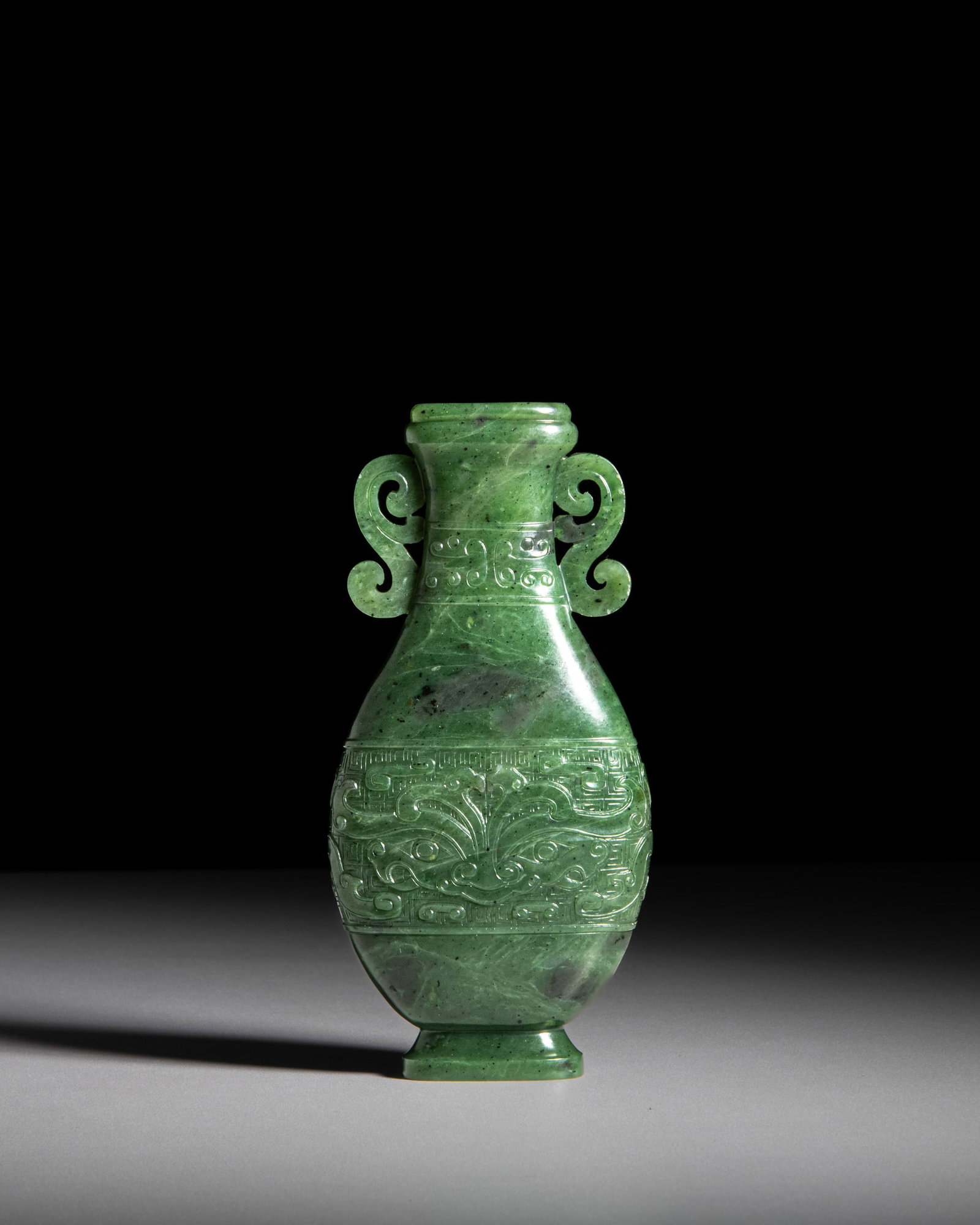 A FINE CARVED SPINACH-GREEN JADE VASE WITH HANDLES, DECORATED WITH TAOTIE MASK MOTIF 清 (1 of 2)
