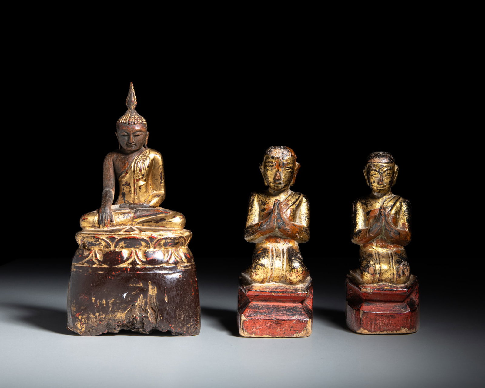 A GROUP OF THREE GILT AND RED LACQUERED FIGURES OF A BUDDHA AND TWO DEVOTEES Burma, late 19th: A GROUP OF THREE GILT AND RED LACQUERED FIGURES OF A BUDDHA AND TWO DEVOTEES Burma, late 19th century H.20.3-15cm