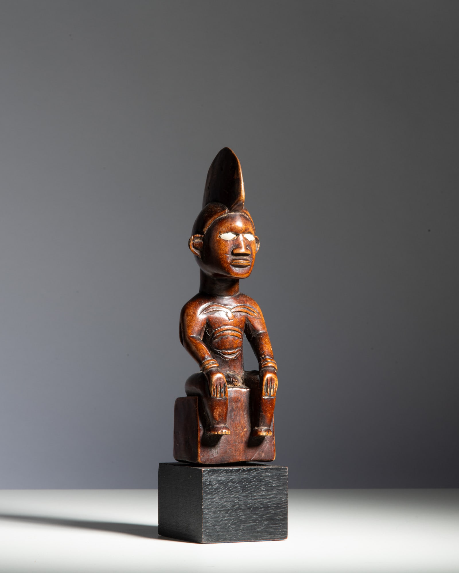 A BEMBE FIGURE Democratic Republic of the Congo Wood and bone Seated on a stylized block-like (1 of 2)