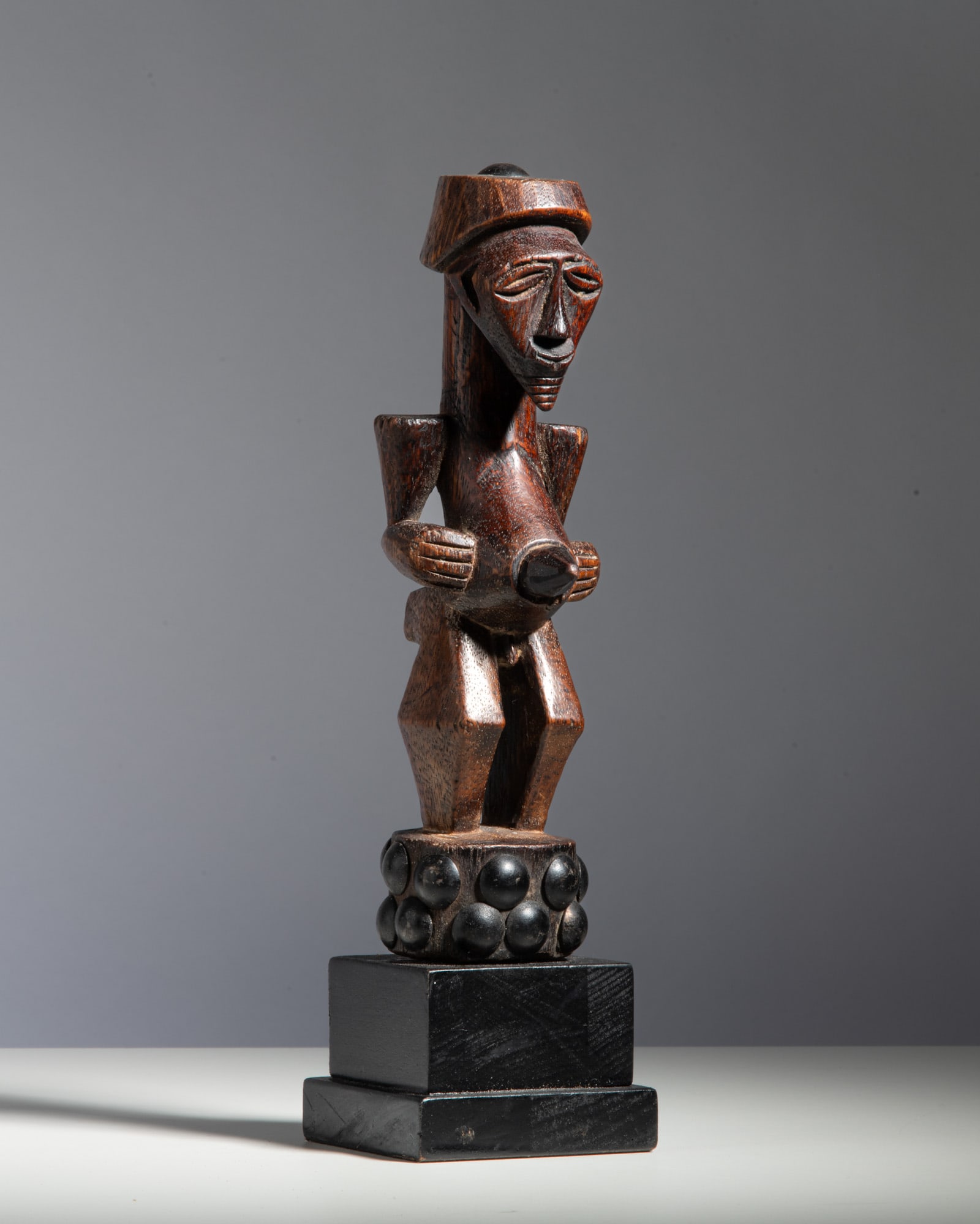 A SONGYE FIGURE Democratic Republic of the Congo Wood This dynamic power figure stands on an: A SONGYE FIGURE Democratic Republic of the Congo Wood This dynamic power figure stands on an unusual, spherical-lobed pedestal base, featuring a classic geometric Songye aesthetic. The angular face is