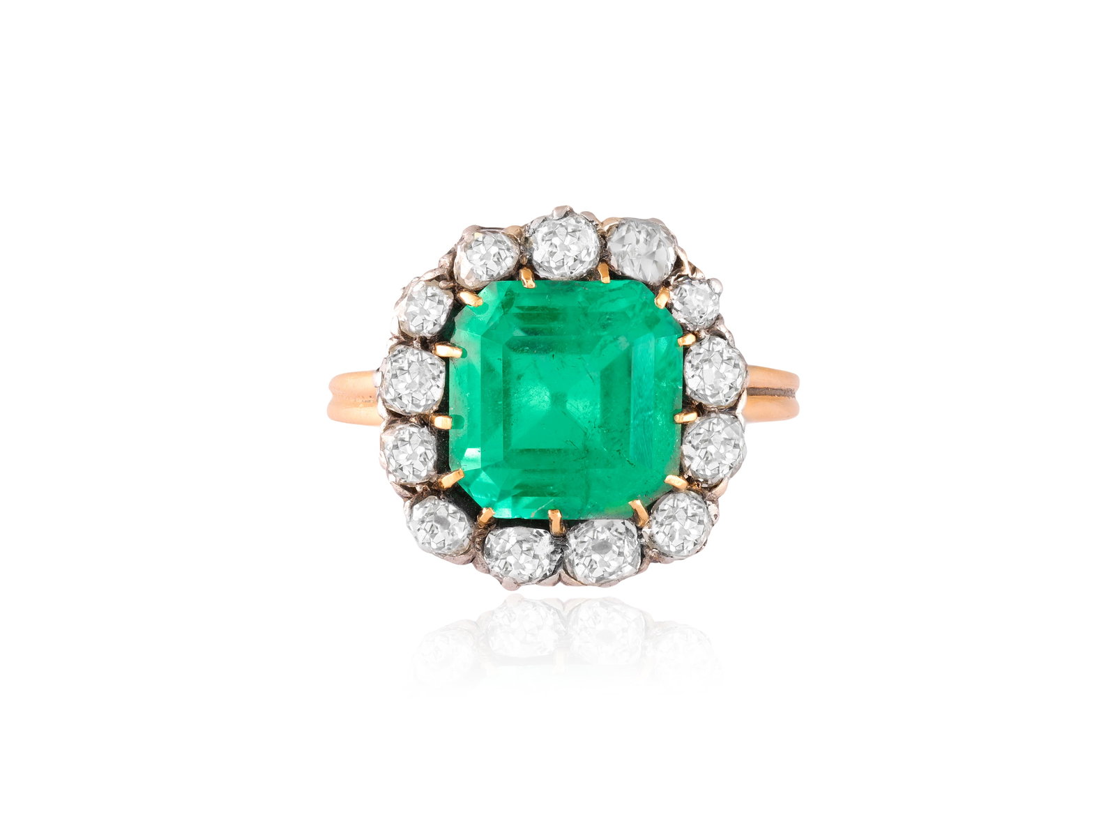 A LATE 19TH CENTURY EMERALD AND DIAMOND CLUSTER RING Set with an octagonal step-cut emerald at the: A LATE 19TH CENTURY EMERALD AND DIAMOND CLUSTER RING Set with an octagonal step-cut emerald at the centre, within an old cushion-shaped diamond frame, to a pierced gallery, mounted in 14K gold and sil