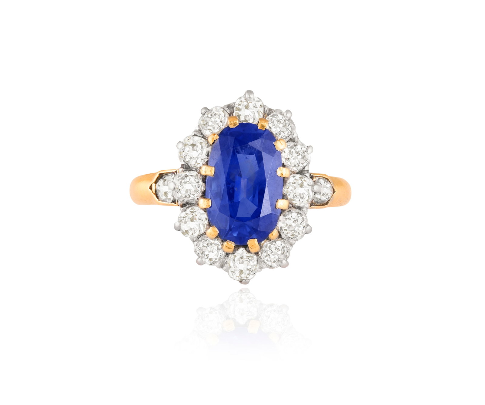 A LATE 19TH CENTURY SAPPHIRE AND DIAMOND CLUSTER RING The elongated oval-shaped sapphire within a: A LATE 19TH CENTURY SAPPHIRE AND DIAMOND CLUSTER RING The elongated oval-shaped sapphire within a multiple-claw setting, to an old-cut diamond surround and similarly-cut diamond shoulders, mounted in 