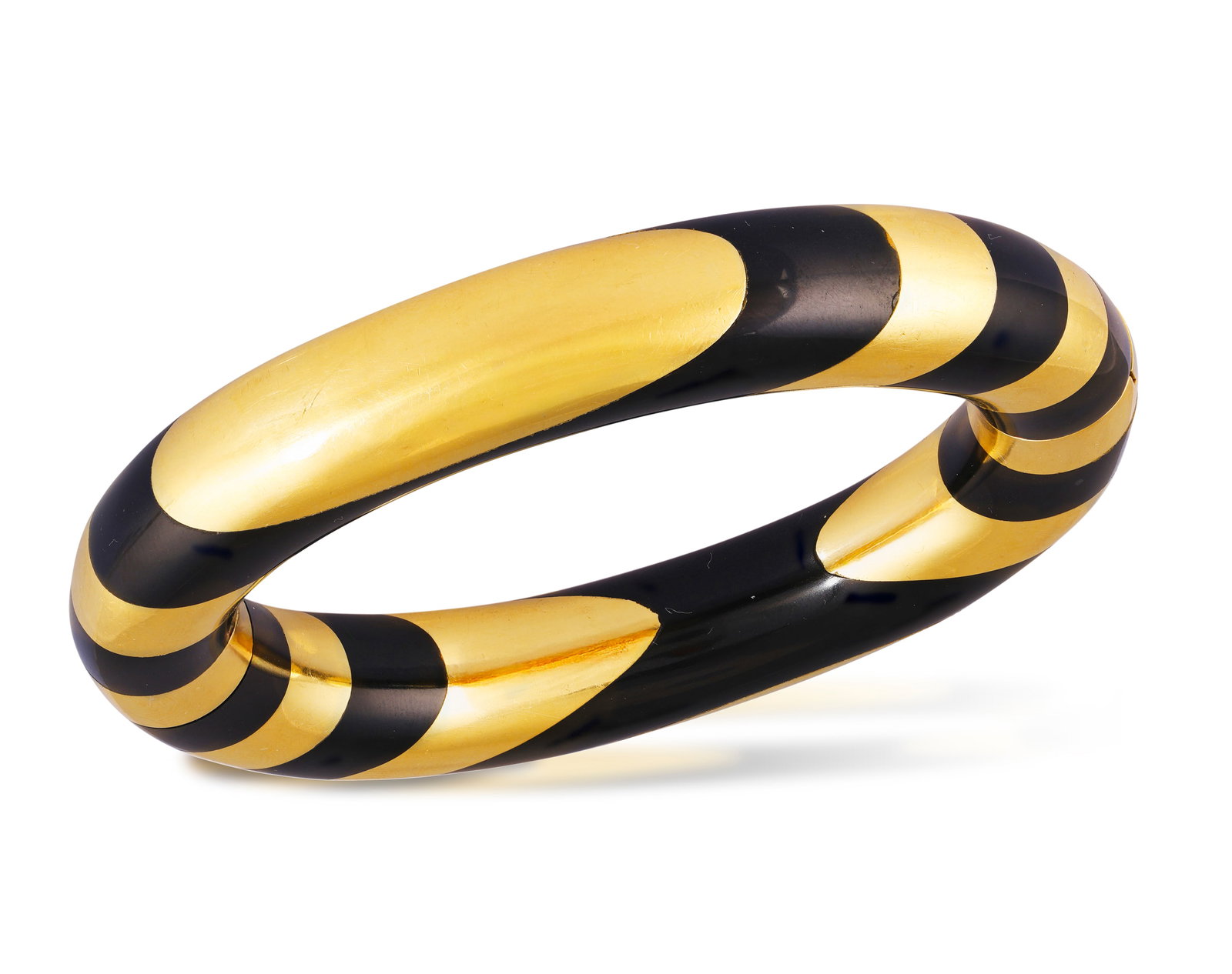 TIFFANY & CO. DESIGNED BY ANGELA CUMMINGS: A COLLECTABLE GOLD AND BLACK JADE BANGLE, CIRCA 1980 The: TIFFANY & CO. DESIGNED BY ANGELA CUMMINGS: A COLLECTABLE GOLD AND BLACK JADE BANGLE, CIRCA 1980 The tapering striped bangle designed with alternating panels of polished black jade and gold, mounted in