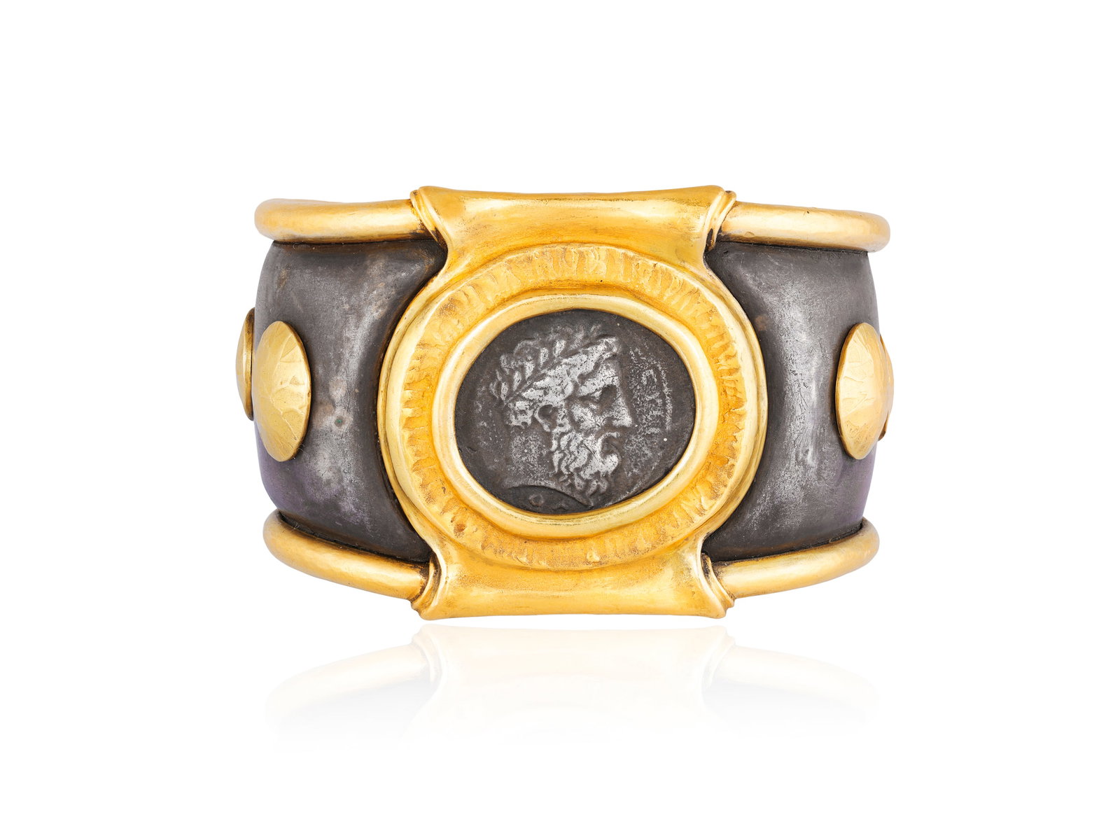 A SILVER GILT CUFF BANGLE Of bi-colour bombé form, the oxidised silver body centred to the: A SILVER GILT CUFF BANGLE Of bi-colour bombé form, the oxidised silver body centred to the front with a circular silver coin depicting a wreathed beaded male in profile, probably Zeus, set within