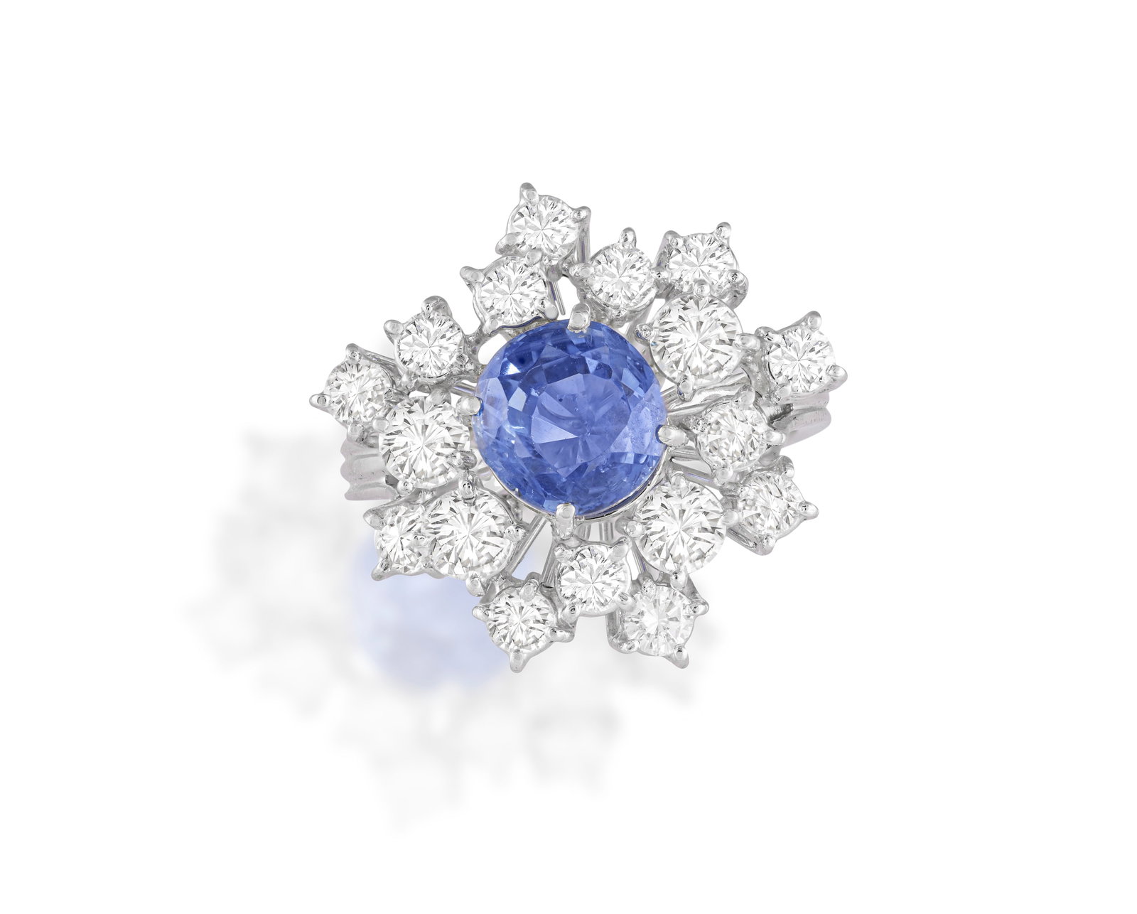 A SAPPHIRE AND DIAMOND CLUSTER RING, CIRCA 1960 Set with a circular-cut sapphire at the centre,: A SAPPHIRE AND DIAMOND CLUSTER RING, CIRCA 1960 Set with a circular-cut sapphire at the centre, within a brilliant-cut diamond surround, to a trifurcated hoop, mounted in 18K gold, diamonds approximat