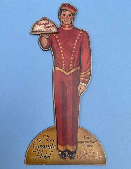 A Grande Hotel Bell hop Masonite sign: A Grande Hotel Bell hop Masonite wood sign measuring 12" inches wide by 24" inches tall.