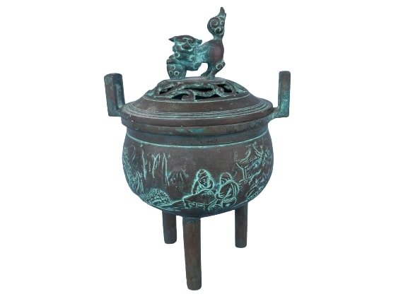 Asian Bronze incense burner: Asian Bronze Incense burner measuring 7 inches tall by 5 inches wide. decorated with a foo dog handle and garden scene with figures.
