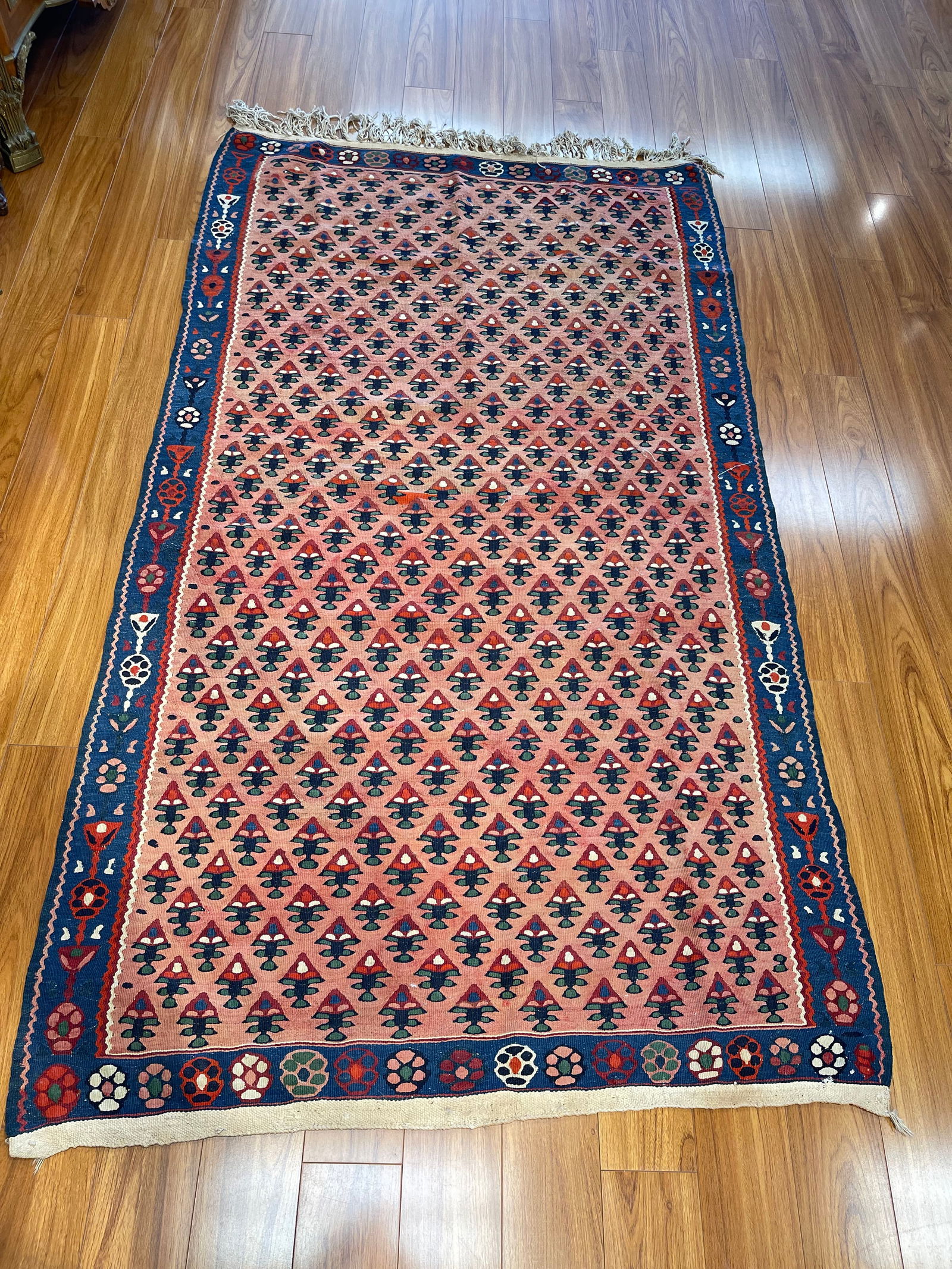 A Persian Kurdish flat woven Kilim rug: A Persian Kurdish flat woven Kilim wool rug measuring 4 feet wide by 7 feet long. A wool handwoven kilim on cotton foundation. This lot was hung on the wall for many decades and has metal ring loops