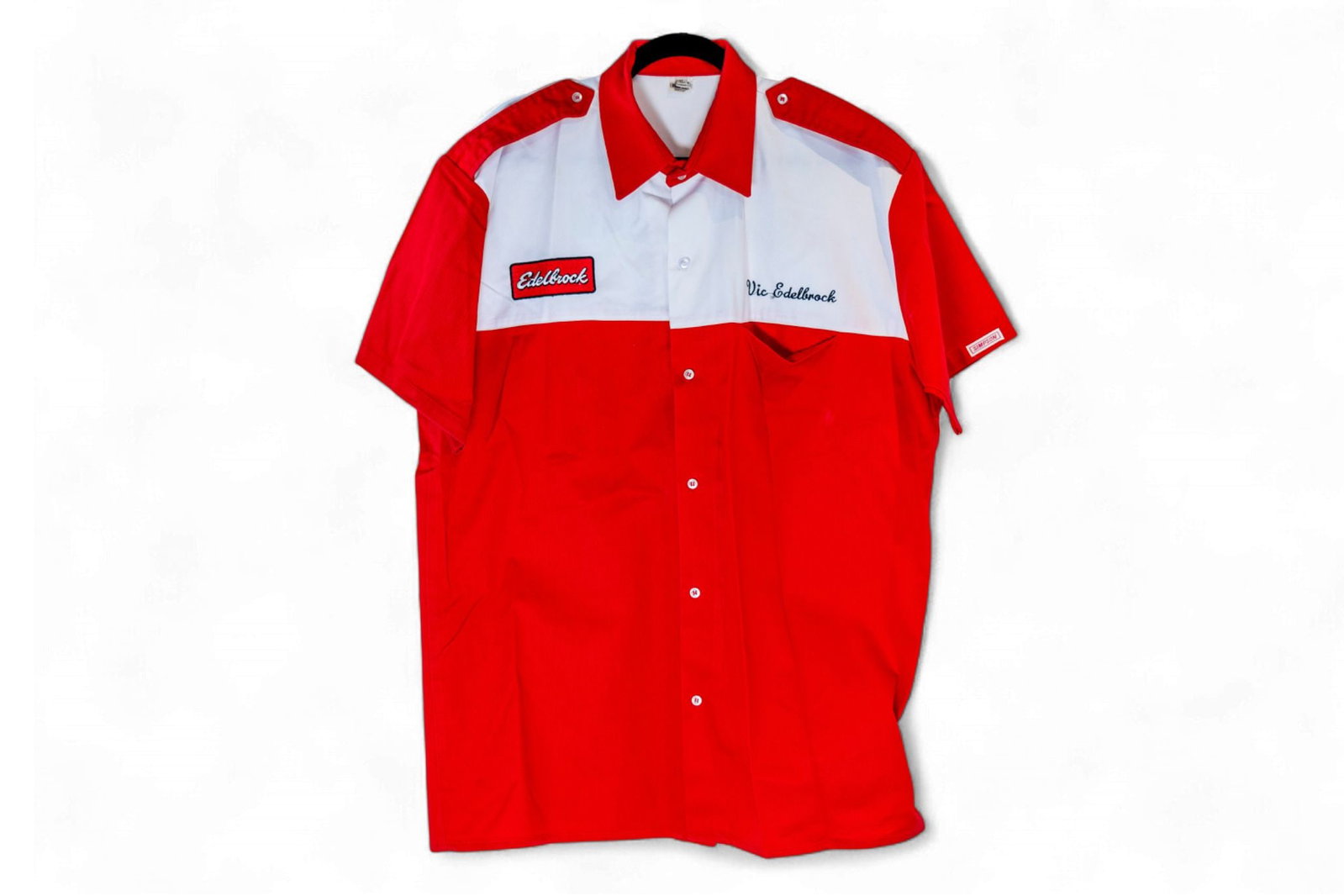 A Vic Edelbrock race team shirt, from the Edelbrock Museum Collection: A Vic Edelbrock race team shirt,cotton poly blend button down shirt by Simpson, red sleeves and white on the top of a red shirt, embroidered Edelbrock patch on right breast and across the shoulders