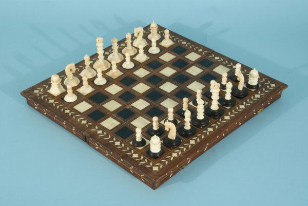 POPPER GAMES COMPANY IVORY CHESS SET: POPPER GAMES COMPANY, NEW YORK CARVED IVORY CHESS SET WITH INLAID EBONY AND IVORY BOARD. Height: 5 in. by Width: 14 in. by Depth: 14 in.