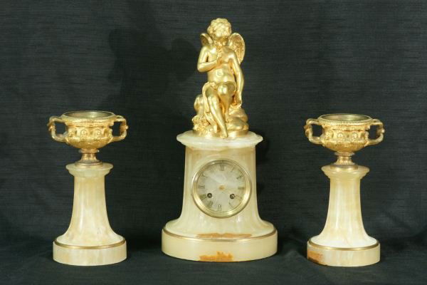 CONTINENTAL GILT BRONZE AND ALABASTER CLOCK SET: THREE-PIECE 19th CENTURY CONTINENTAL GILT BRONZE AND ALABASTER CLOCK SET (CLOCK IS NOT IN WORKING ORDER, AS IS.) CLOCK IS MOUNTED WITH WINGED CUPID AND PAIRED WITH GILDED BRONZE GREEK HERO CUPS MOUNTE