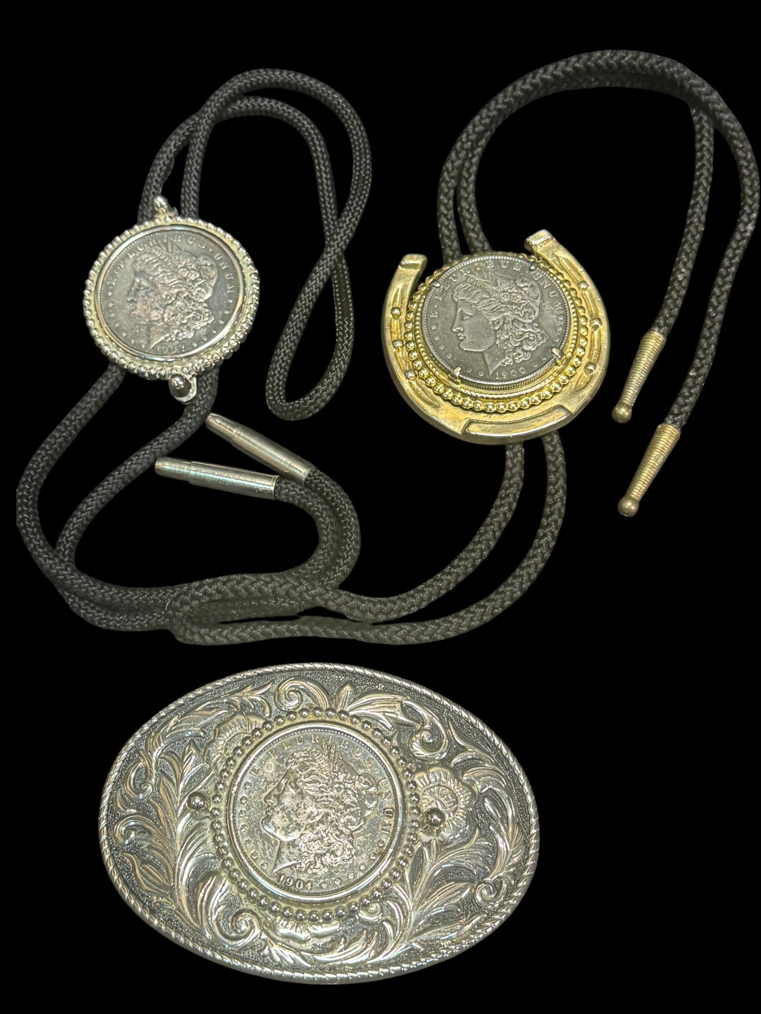 TWO BOLO TIES & BELT BUCKLE WITH MORGAN DOLLARS: TWO BOLO TIES AND A BELT BUCKLE WITH MORGAN DOLLAR COINS SET IN EACH PIECE.