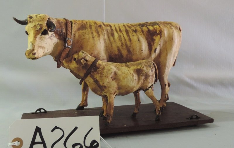 Cow and calf mounted on wheels with leather colla.: Antique Cow and calf mounted on wheels with leather collars. They are on a wire frame with hide over them. Calf missing a leg. Cow’s neck split.