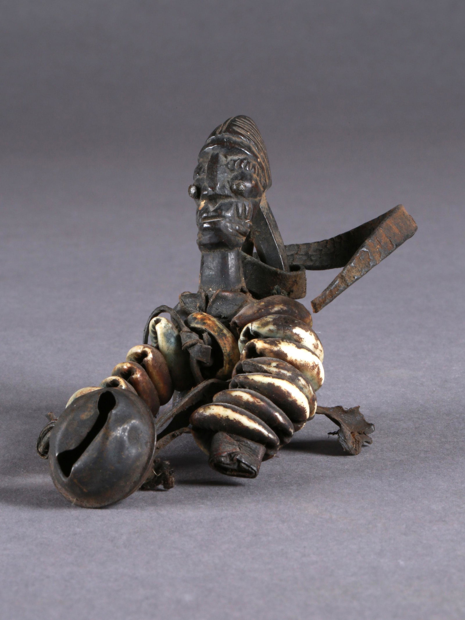 A Yoruba Wrist Pendant, "ogo elegba": Handgelenk-Anhänger, "ogo elegba" Yoruba, Nigeria Ohne Sockel / without base Holz, Leder, Kaurischnecken. H 7,5 cm (nur die Figur) L 11 cm (mit Kette und Glocke) Provenienz: W. Häusler (Thurgau), 19