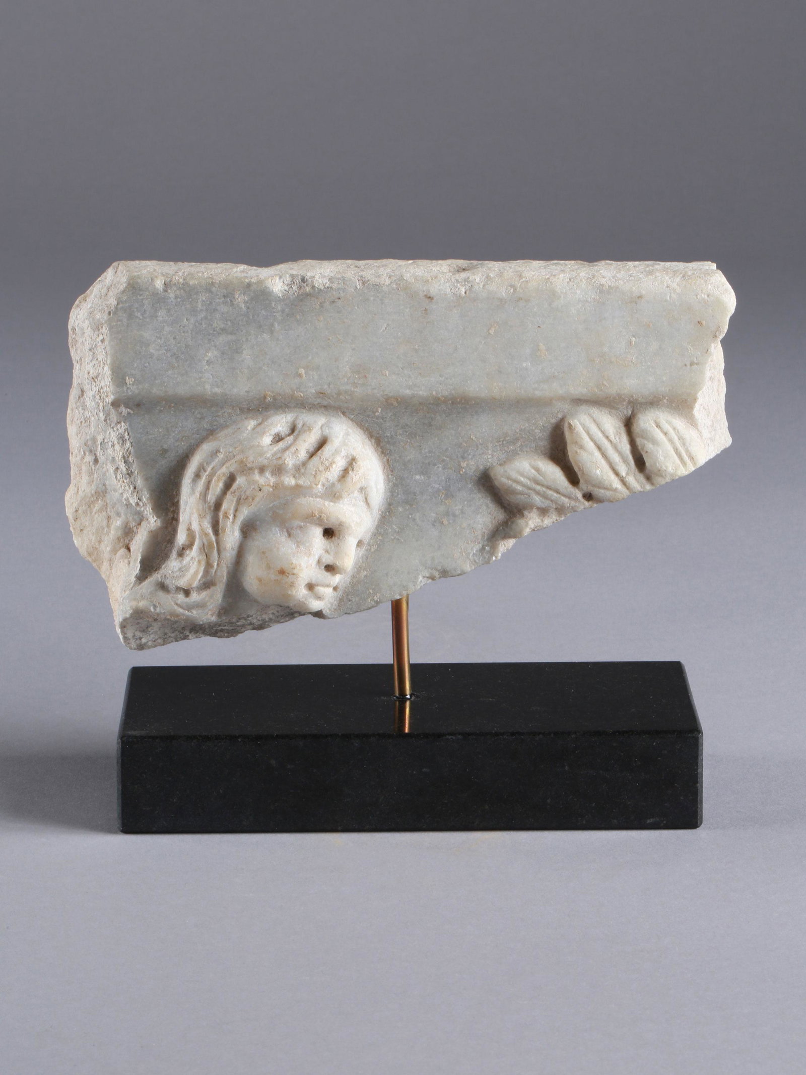 Piece of a Sarcophagus with the Face of a Child: TEIL EINES SARKOPHAGS MIT KINDERKÖPFCHEN Mittelmeerraum Ohne Sockel / without base Stein. B 19 cm. Provenienz: Galerie Serodine, Ascona. CHF 200 / 400 EUR 172 / 344
