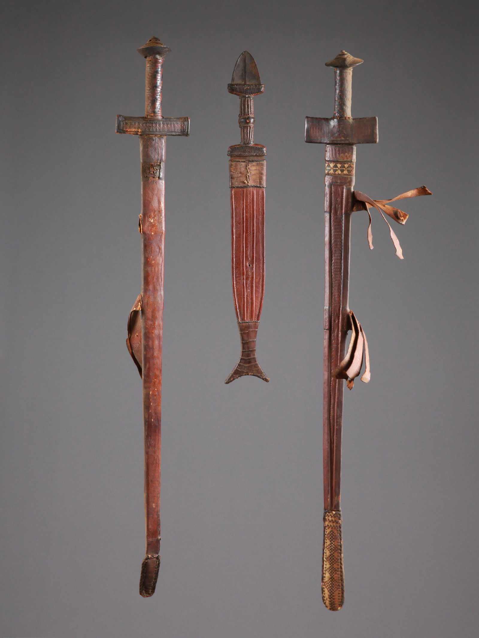 2 Tuareg Swords and a Dagger, all with Sheaths: 2 Schwerter und ein Dolch, alle mit Scheide Tuareg, Sahelzone Ohne Sockel / without base Holz, Eisen, Bronze, Leder. L 51 - 91 cm. Provenienz: - Société des missionnaires d’Afrique, P&