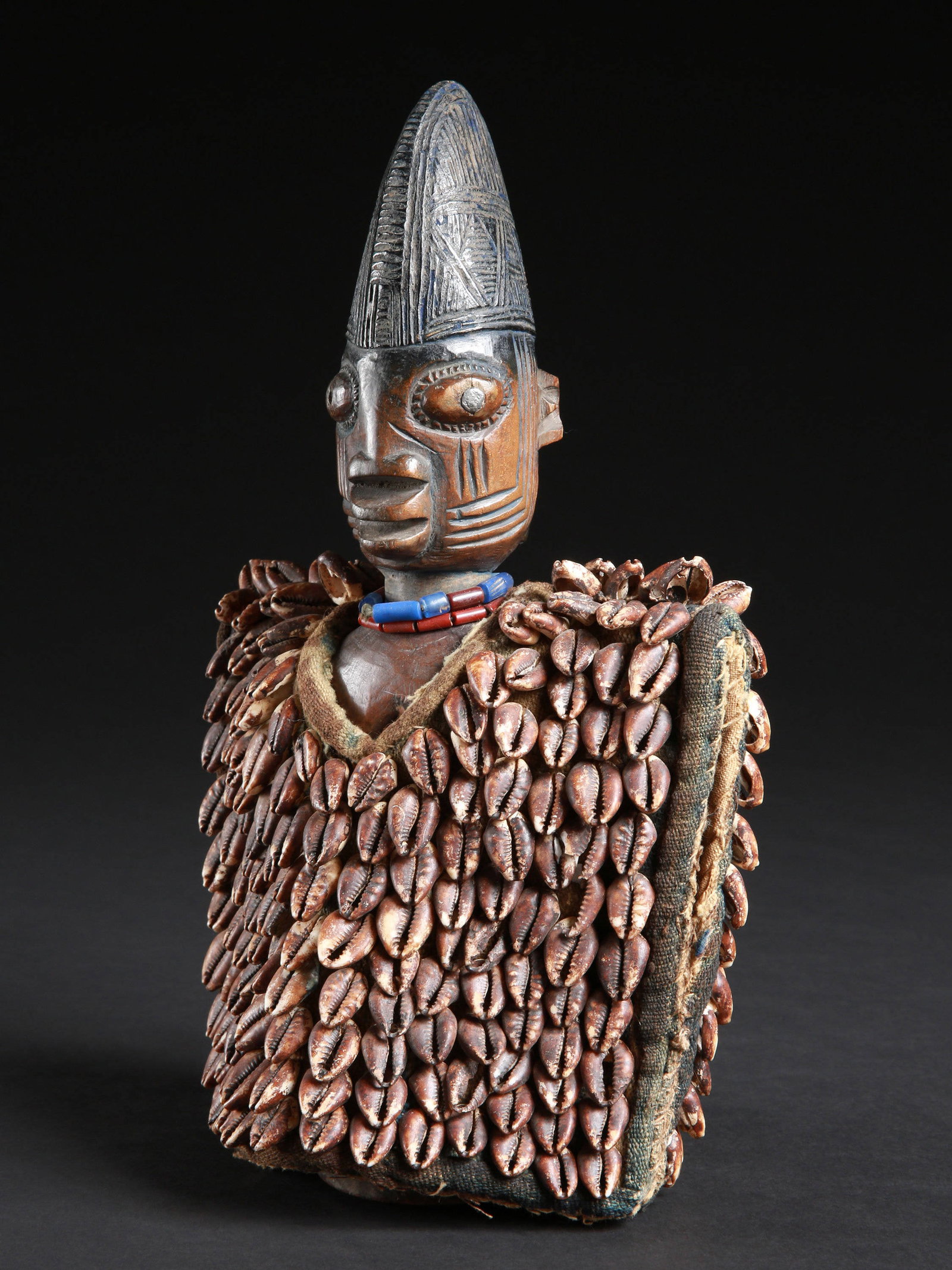 A Yoruba Twin Figure, "ere ibeji", with Garment: Zwillingsfigur mit Kleid, "ere ibeji" Yoruba, Nigeria Ohne Sockel / without base Holz, Textil, Glasperlen, Kaurischnecken. H 30.5 cm. Provenienz: Beatrice Leutert und Marcel Plüss, Thurgau, Schwe