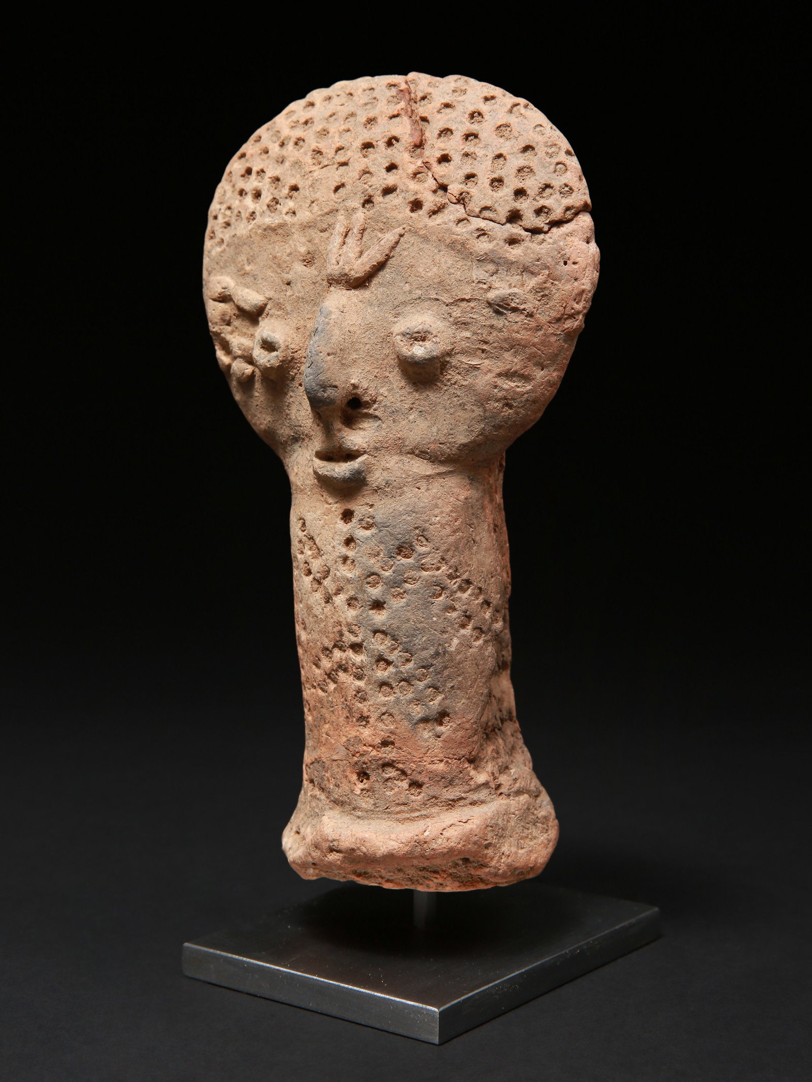 A Bura-Asinda-Sikka anthropomorphic Head: Anthropomorpher Kopf Bura-Asinda-Sikka Kultur. Niger Mit Sockel / with base Terrakotta. H 18,5 cm. Provenienz: Schweizer Privatsammlung, Basel. Kopf einer phallischen Tonglocke, die als Grabwächt