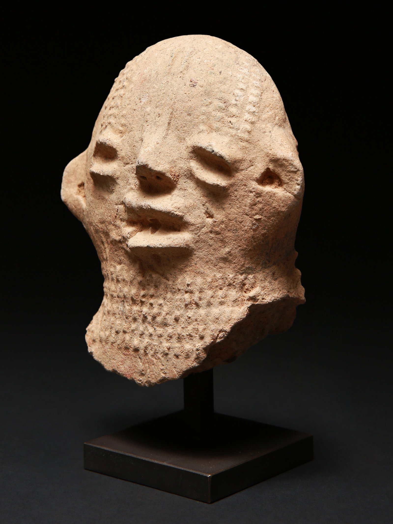 A Bura-Asinda-Sikka anthropomorphic Head: Anthropomorpher Kopf Bura-Asinda-Sikka Kultur. Nigeria Mit Sockel / with base Terrakotta. H 12 cm. Provenienz: Schweizer Privatsammlung, Basel. Kopf einer phallischen Tonglocke, die als Grabwächt