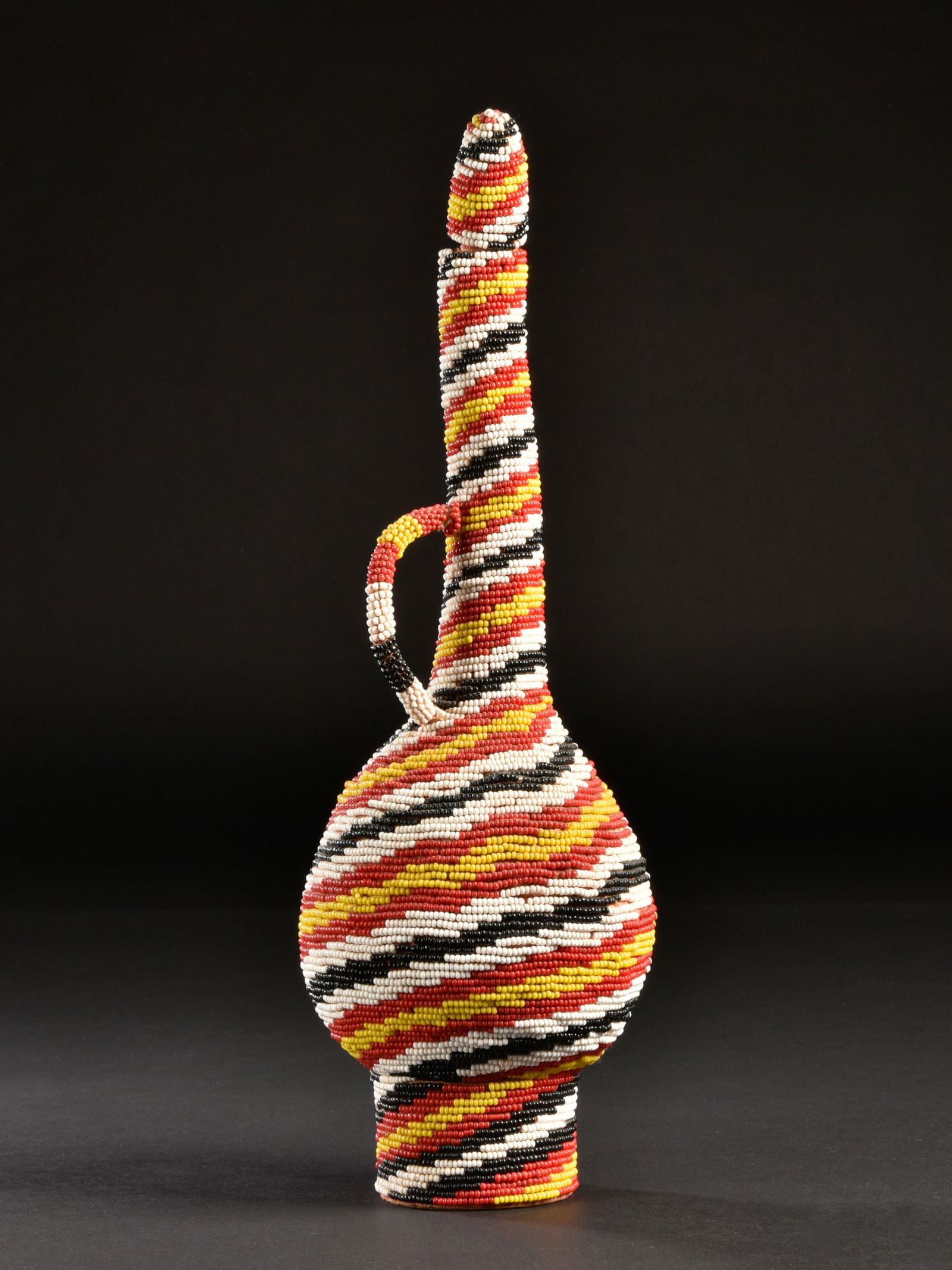 A Beaded Bottle with Handle: Mit Glasperlen verzierte Henkelflasche Kamerun Ohne Sockel / without base Kalebasse, Glasperlen. H 33 cm. Provenienz: - Galerie Walu, Basel (vor 1969). - R. Bischoff, Basel. - Hammer Auktionen,