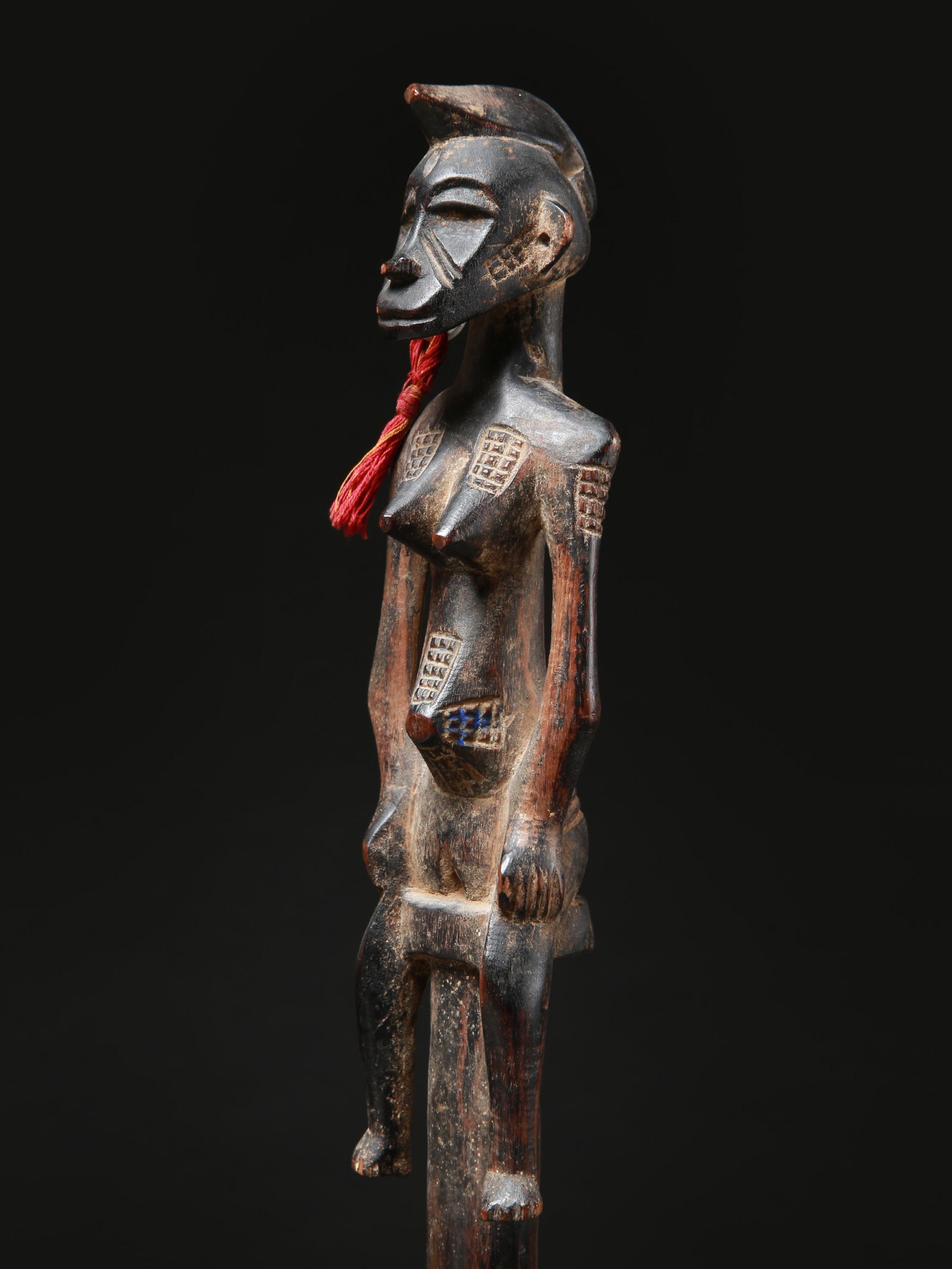 A Senufo Staff with a seated female Figure, "tefalipitya": Stab mit sitzender Frauenfigur, "tefalipitya" Senufo. Côte d’Ivoire Mit Sockel / with base Holz, Weissmetall, Textil. H 109 cm. Provenienz: - Walter Moser, Zürich. - 2012: André K