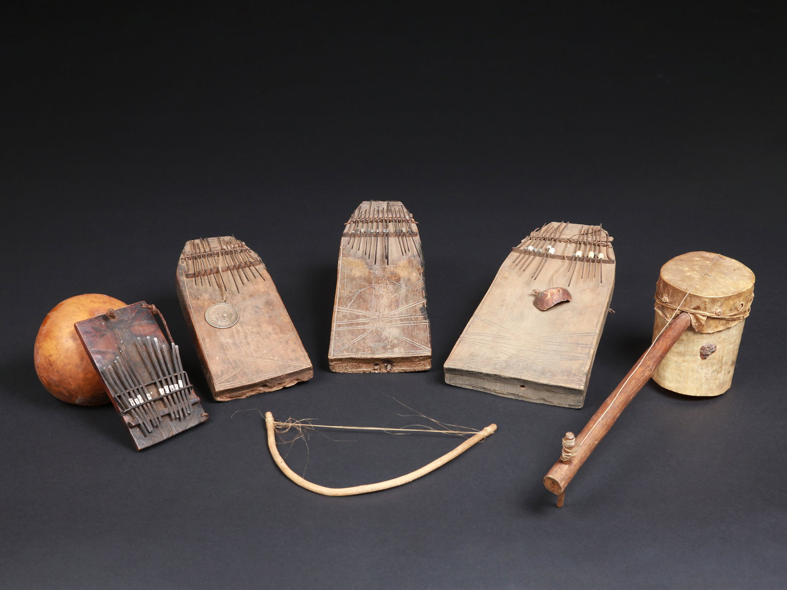 4 Lamellaphones ("Thumb pianos") and a Fiddle, "iningira": 4 Lamellophone und ein Streichinstrument, "iningira" Tansania / Ruanda Ohne Sockel / without base Holz, Eisen, Leder, Kalebasse. H 25 - 41 cm. Provenienz: - Primus und Veronika Monn (1940-2006 / 1941-