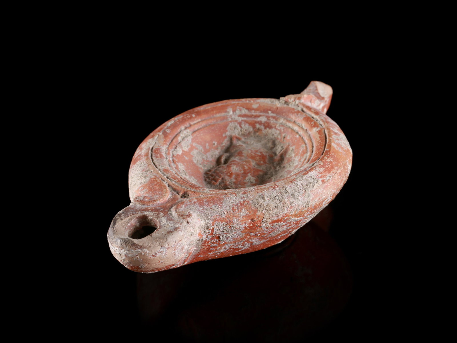A Roman Oil Lamp with a Silenus Head: Öllampe mit Silenskopf Römisch Ohne Sockel / without base Terrakotta. H 2,5 cm. B 6,5 cm. L 10,5 cm. Provenienz: - Schweizer Privatsammlung (von 1970). - Schweizer Privatsammlung, Basel.