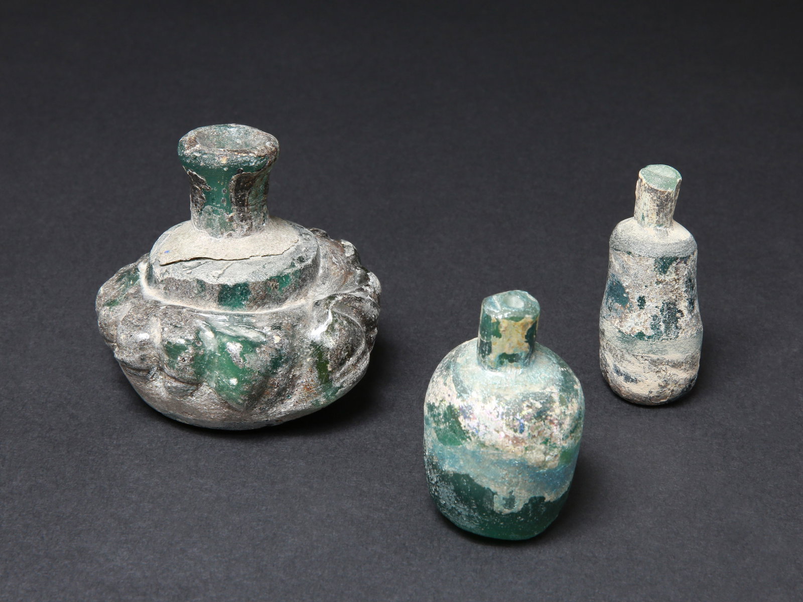 3 Roman Glass Bottles: 3 Glasfläschchen Römisch Ohne Sockel / without base Glas. H 6 - 7 cm. Provenienz: Schweizer Privatsammlung, Basel. CHF 300 / 600