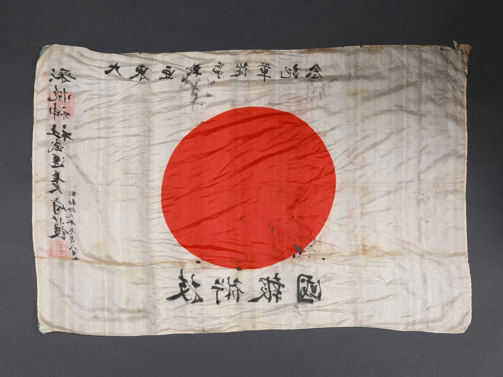 A Japanese Good Luck Flag from WWII, "yosegaki hinomaru": Glücksflagge, 2. Weltkrieg, "yosegaki hinomaru" Japan Ohne Sockel / without base Seide. B 69 cm. L 101 cm. Provenienz: - Donley Auctions, Auction Sale 109, June 2020. - Schweizer Privatsammlung, Base