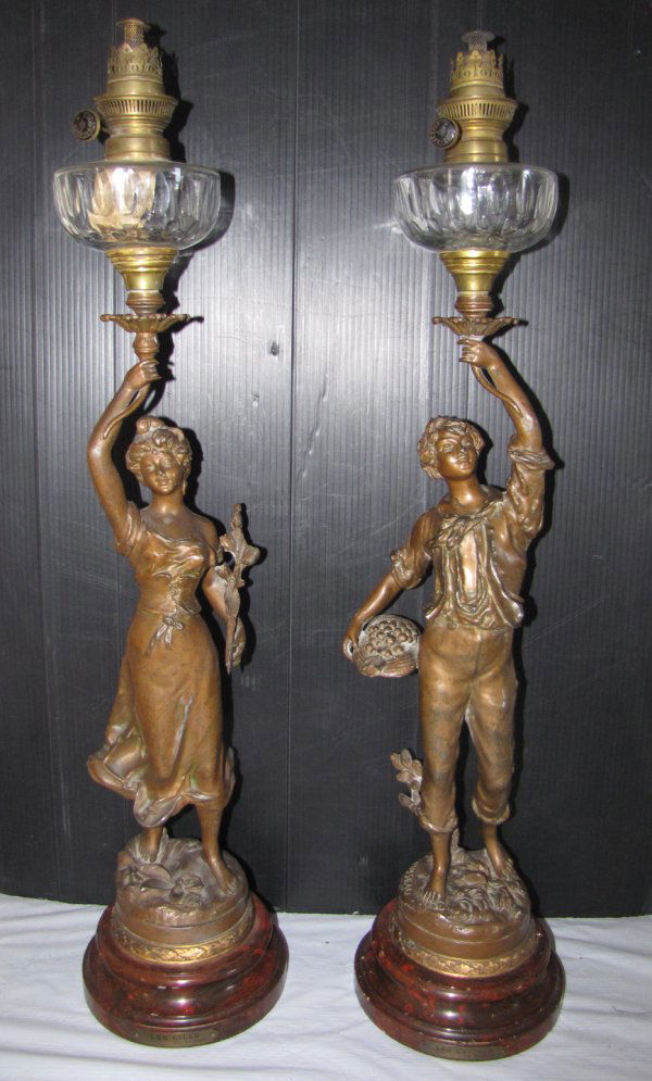 SGND: ROUSSEAU PR OIL LAMPS OF LADY AND MAN 3414: Pair of signed Rousseau bronze toned figural oil lamps with marblized metal bases. Plaques on the front of each read, on the woman "Les Lil'as" (Lilacs) and the man "Les Cerises" (Cherries). Dimension