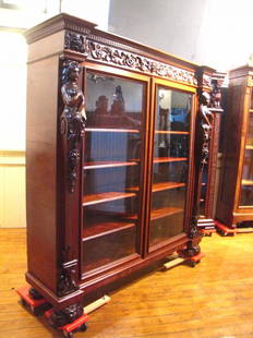 ANTQ 2 DOOR CARVED MAHOGANY BOOKCASE W/ LADIES 3470: Elaborate two door carved mahogany bookcase with lady supports, carved frieze with lady and men faces, winged phoenix and lion heads. Dimensions: 66"H x 65"W x 18.5"D Age: 1880 Material: Mahogany