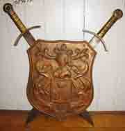 SM BRASS SHIELD W/ CROSS SWORDS & FAMILY CREST 15672: Small brass shield w/ cross swords w/ knight bust & family crest Dimensions: Age: Material: Brass