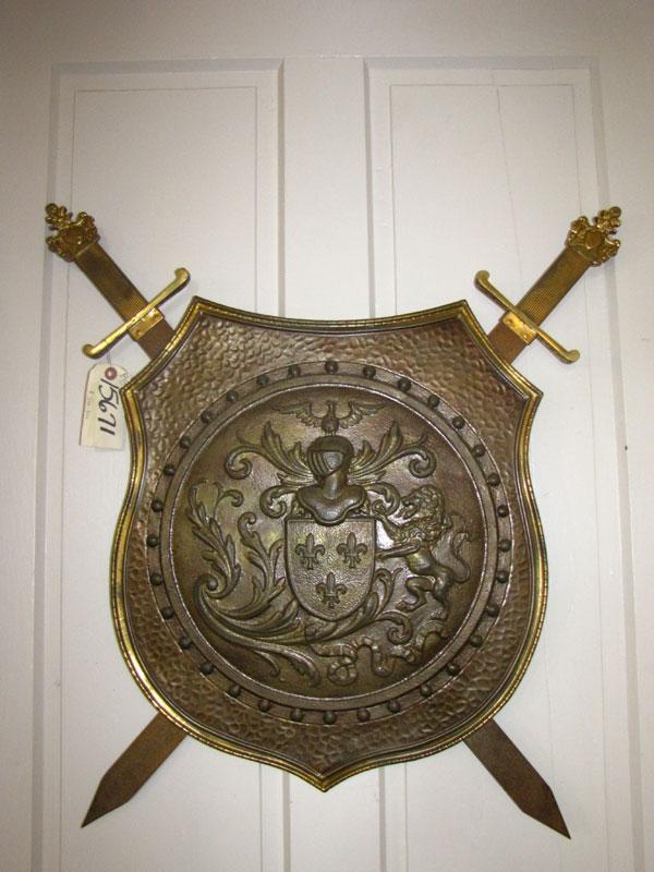 BRASS WALL SHIELD W/ CROSSED SWORDS (15671): Brass decorative wall shield with crossed swords. Dimensions: 28"H x 26"W Age: 1900 Material: Bronze