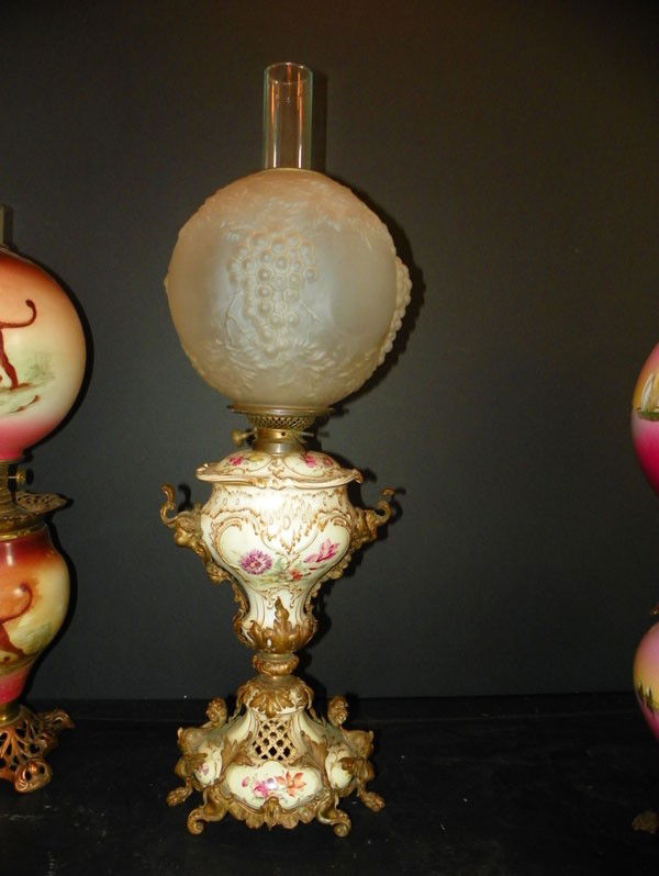 BZ AND PORC OIL LAMP 2193: Figural bronze and porcelain oil lamp with winged lady and cupid heads floral painted porcelain and pierced porcelain. Signed EM Dupley Base Co. Dimensions: Shade: 52"H x 9.5" Diameter Without glass: